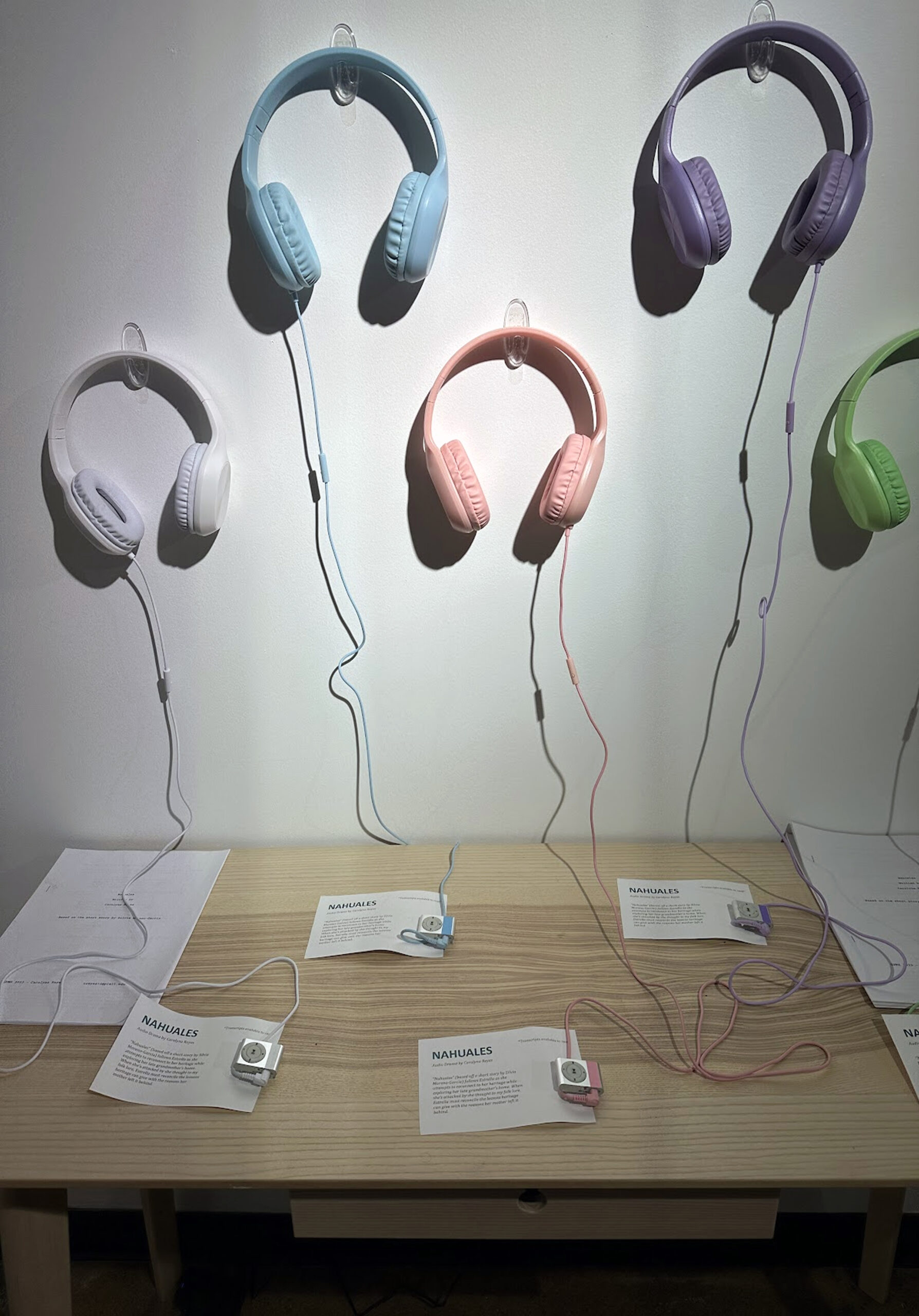 headphones of various colors, on wall, with table under the headphones, with pamphlets