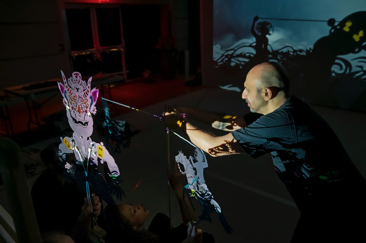 A man holding a stick that controls an elegantly designed shadow puppet.