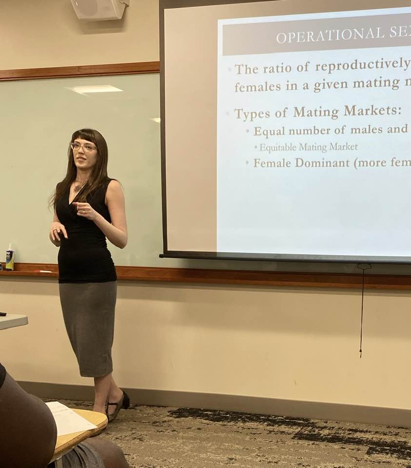 woman standing at blackboard projector, speaking