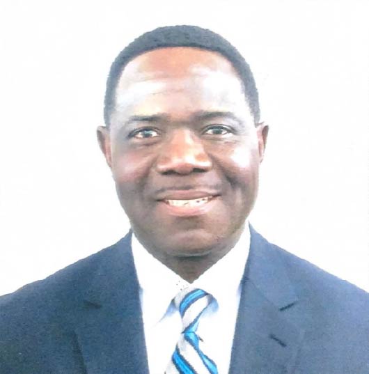 Formal headshot of a man wearing a dark blue suit, white shirt, and blue striped tie, smiling against a plain white background.