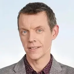 Headshot of a man with short brown hair wearing a gray jacket and patterned shirt, posing against a light background.