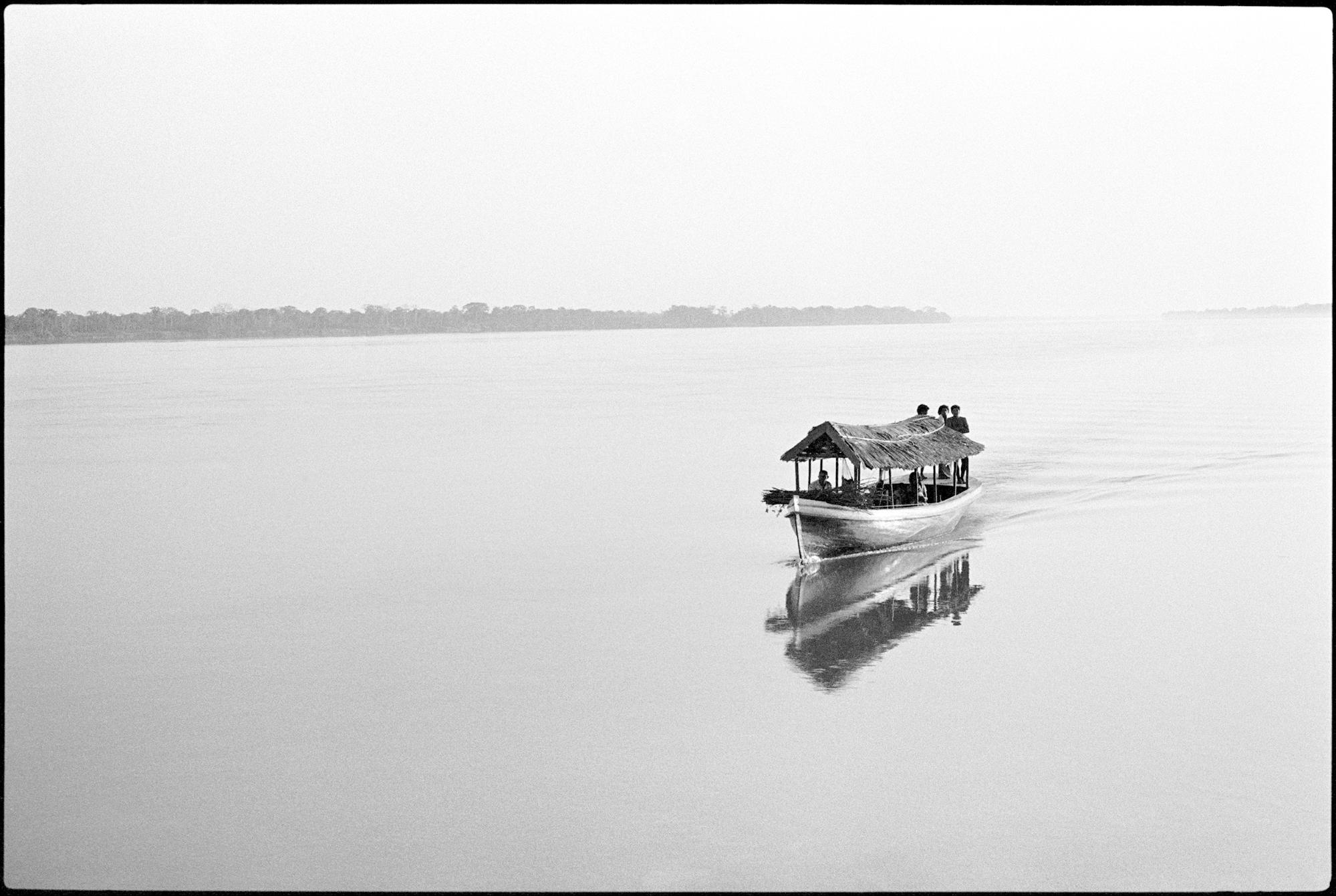 boat with straw roof, coasting on river or lake, black and white image, water is very reflective, showing the boat and the sky