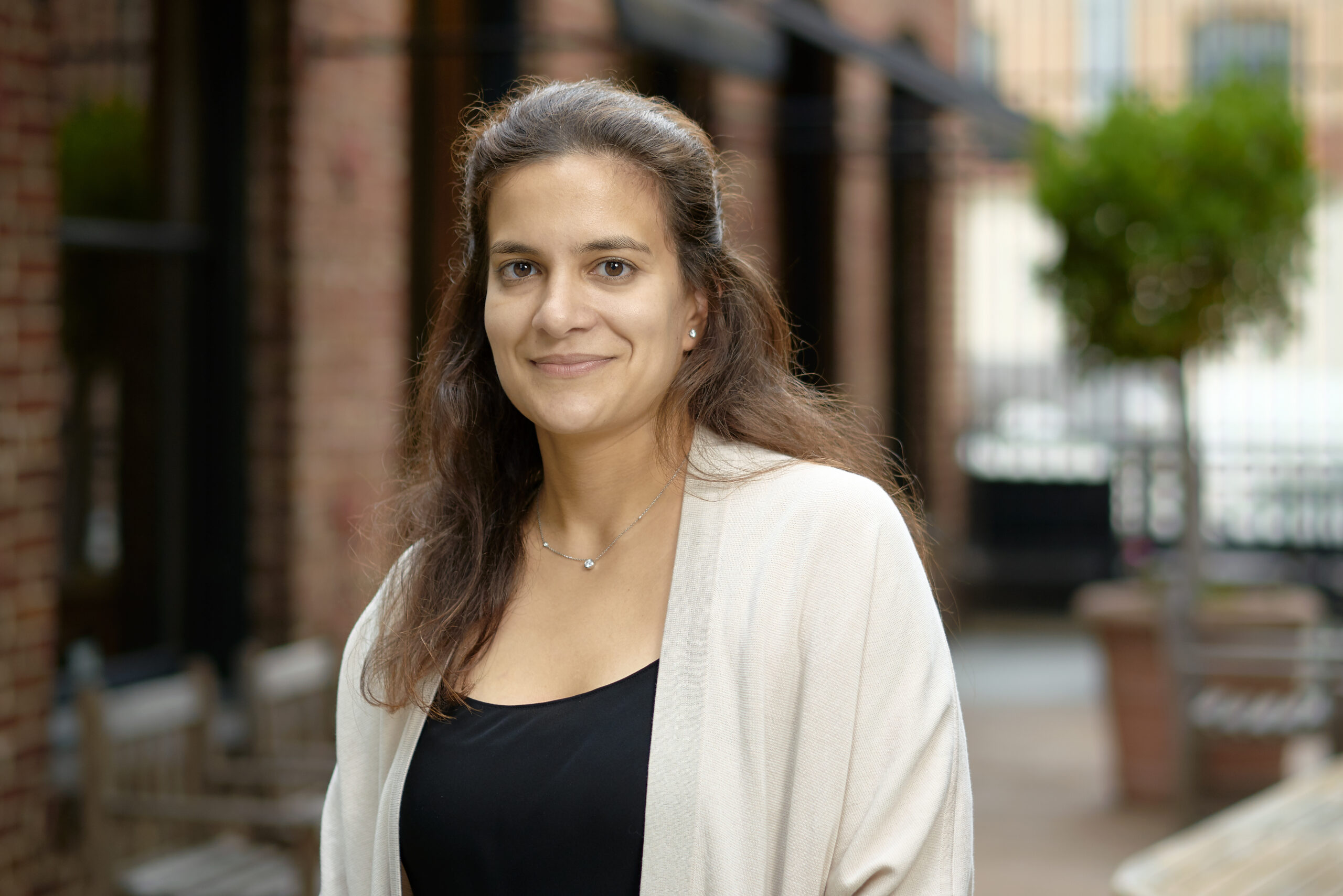 A headshot of a woman in a white blazer in front of a brick building.