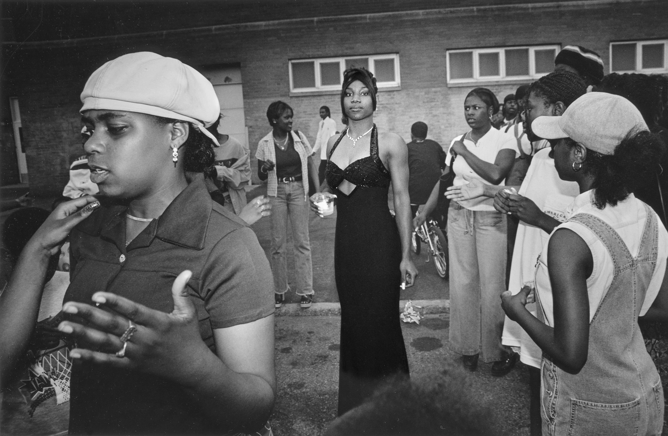A photograph of a gathering of young people of color, with one person in the center of the photograph wearing a black dress.