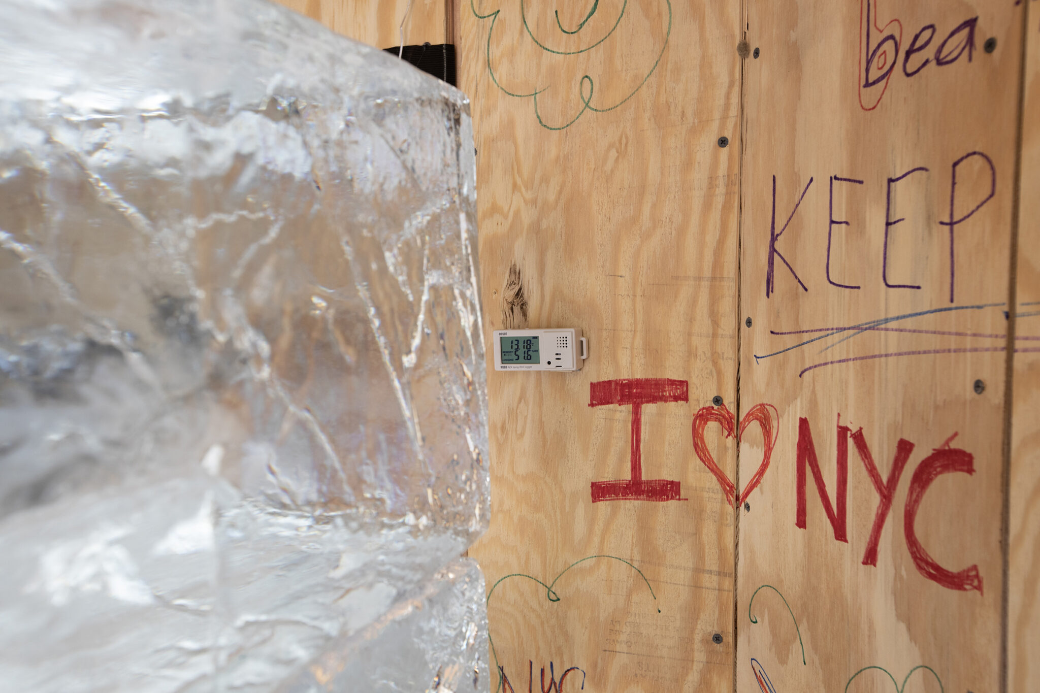 Large block of ice sits in front of wood structure wall with messages like I Heart NYC in marker