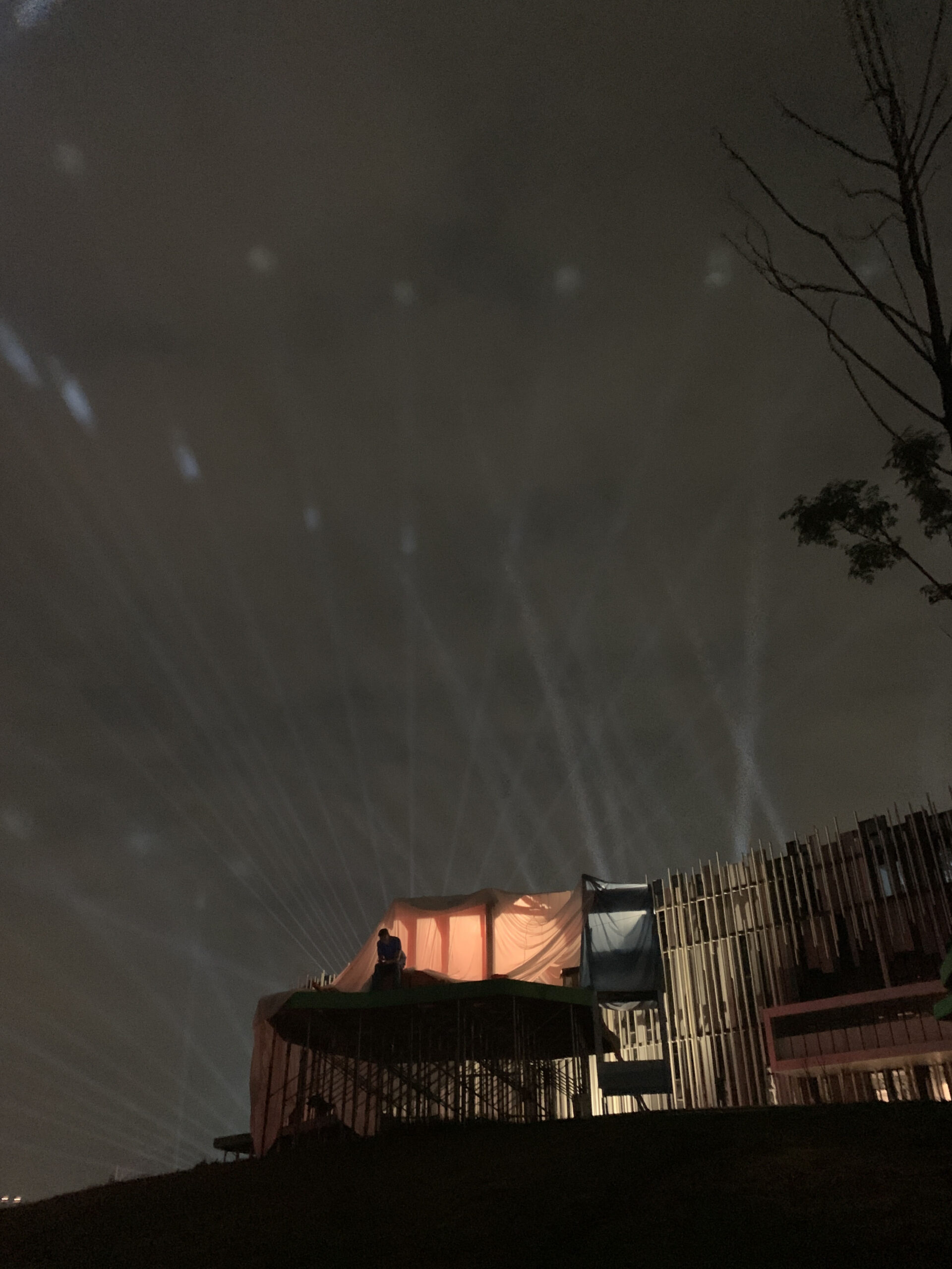 Beams of light shoot through the sky above a tent structure lit from within