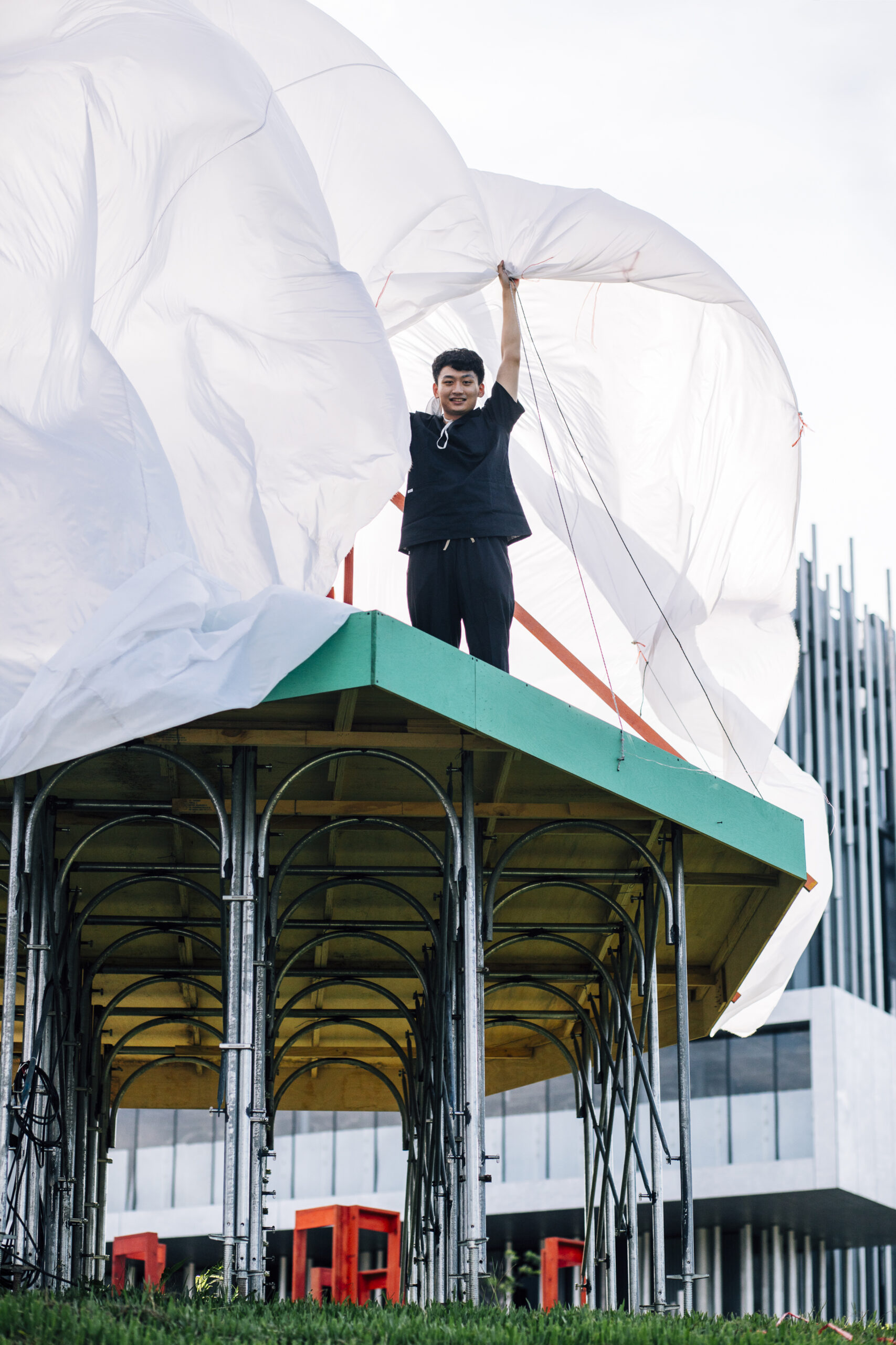 Person in black top and pants stands on green platform holding large billowing white sheet overhead