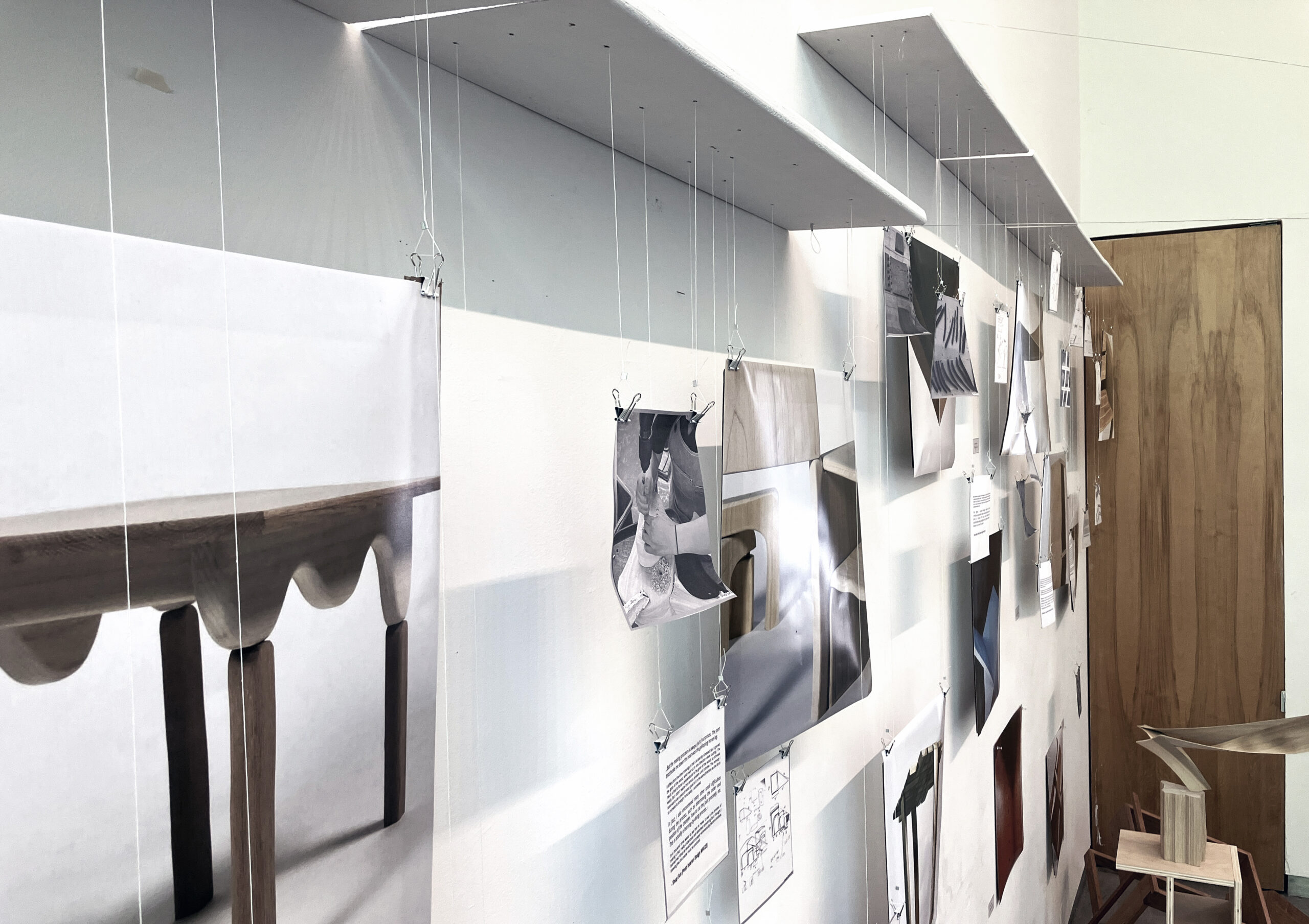 Gallery wall with photos and didactics hung with white thread and binder clips from panels protruding from wall