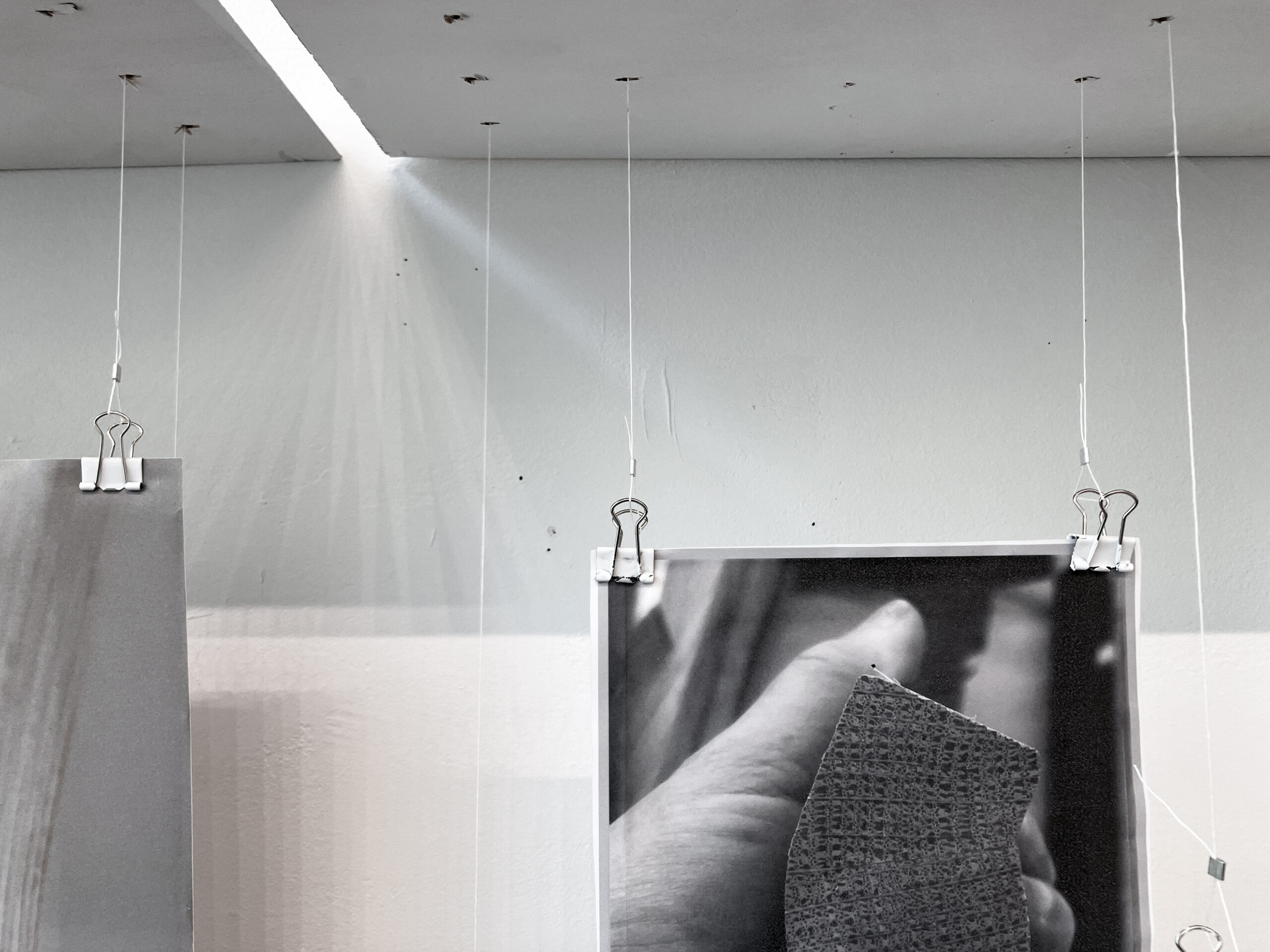 Close view of photo installed suspended with string and binder clips, showing hand holding wood with detail of grain