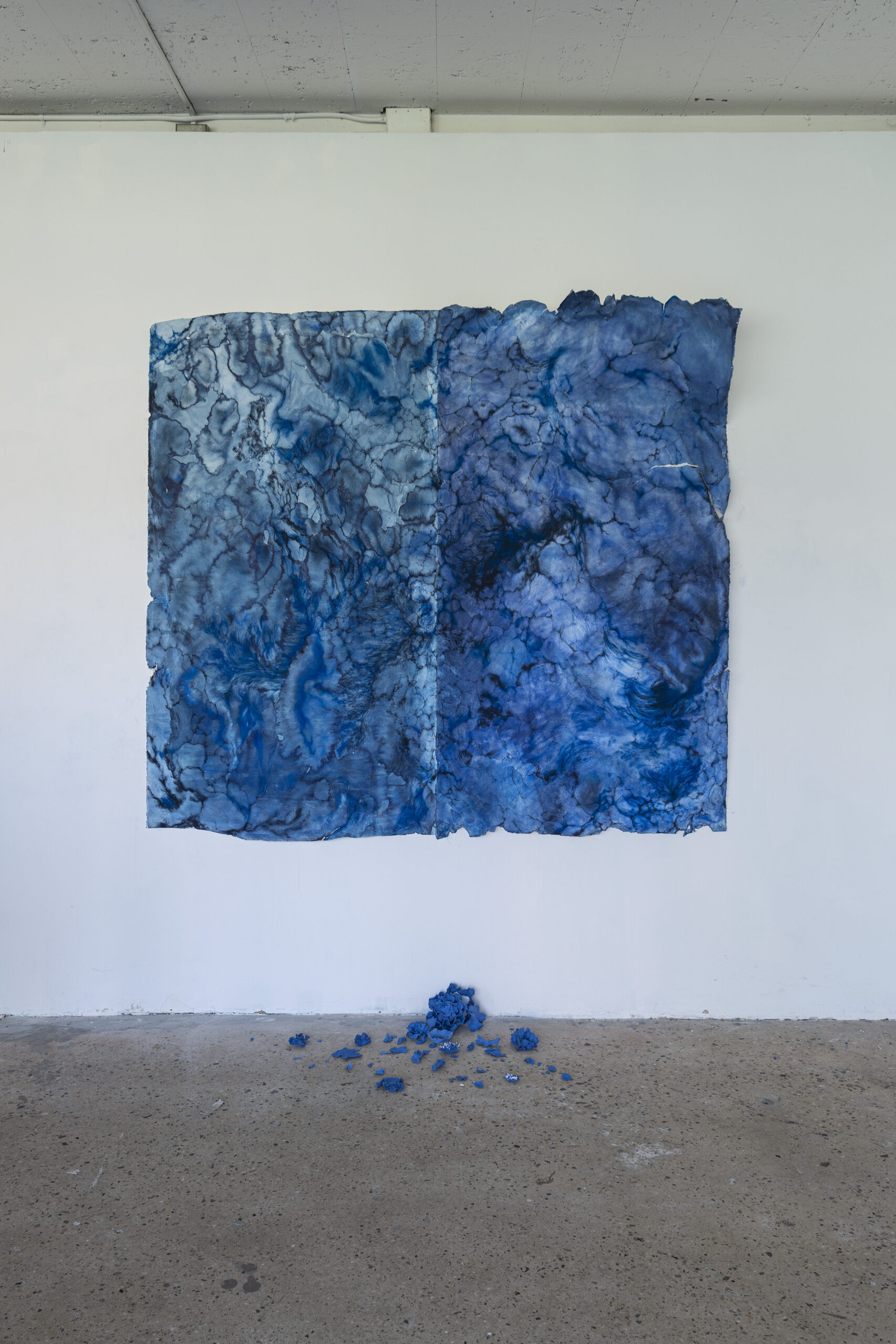 image of a drawing, in a gallery room, with blue fabric pieces scattered on the floor