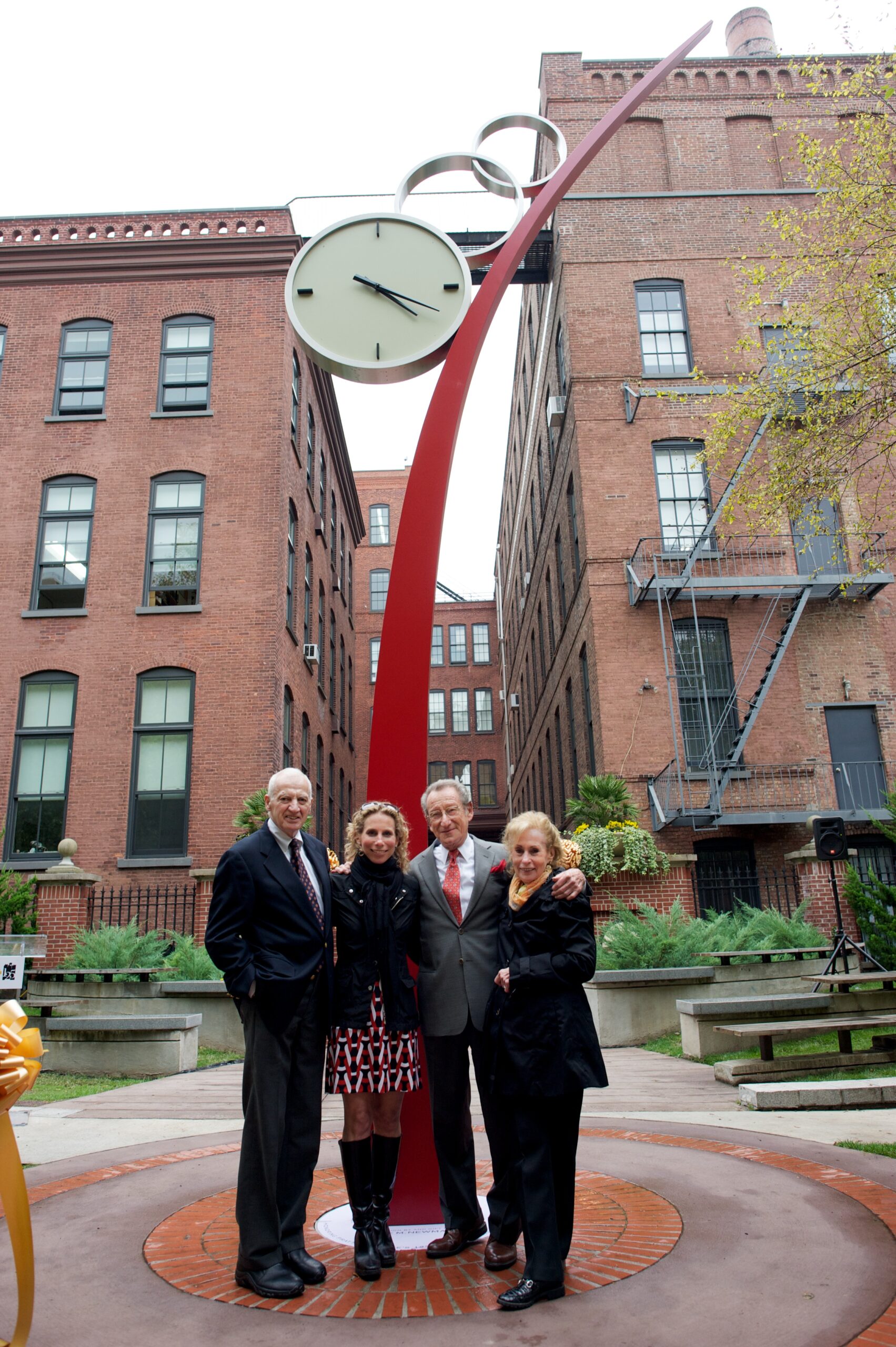 Four adults in business attire pose in front of tall, sculptural red clock