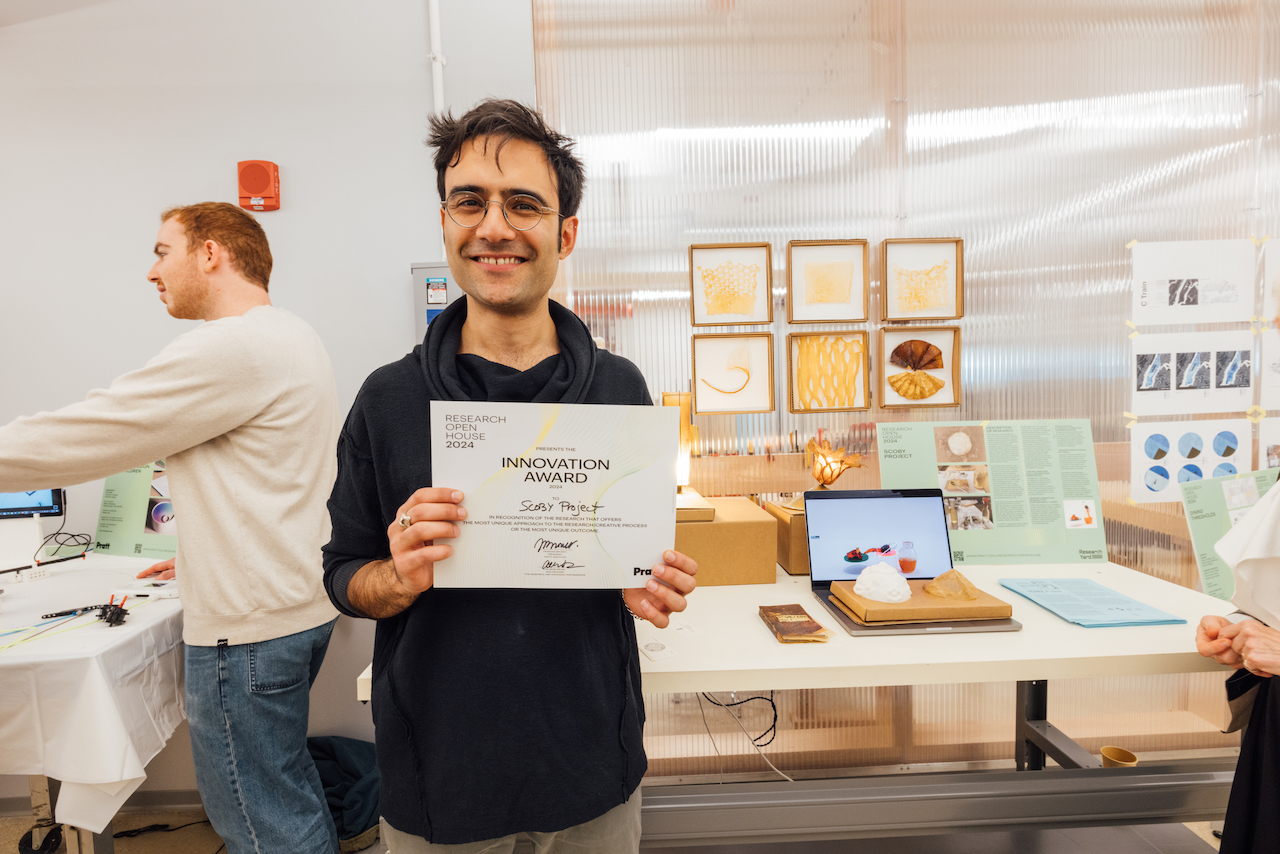 student, smiling, holding award documentation, with desks and office in background