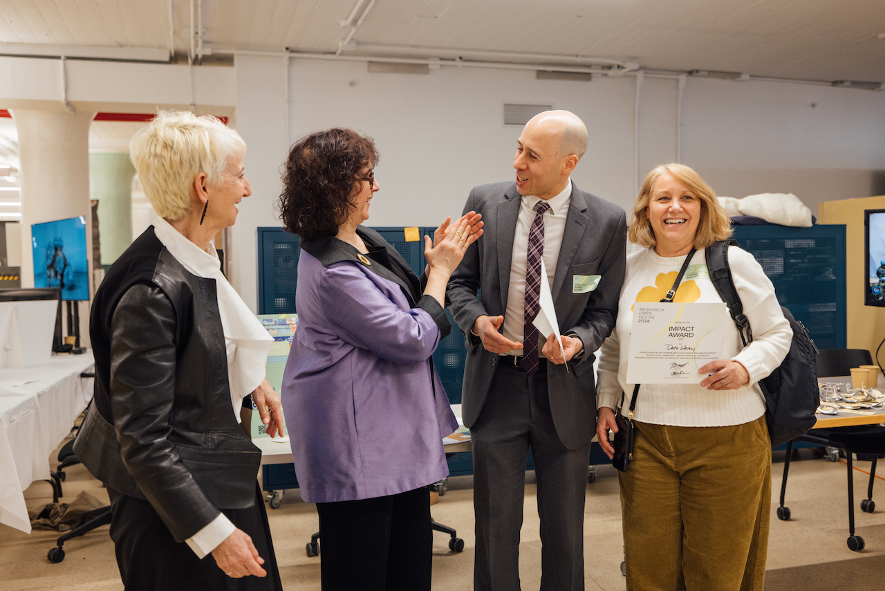three faculty members, smiling, standing with president Bronet, with offices in background