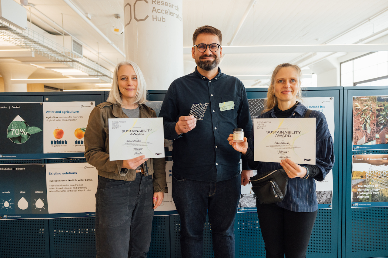 three students, smiling, holding award documentation, with desks and office in background