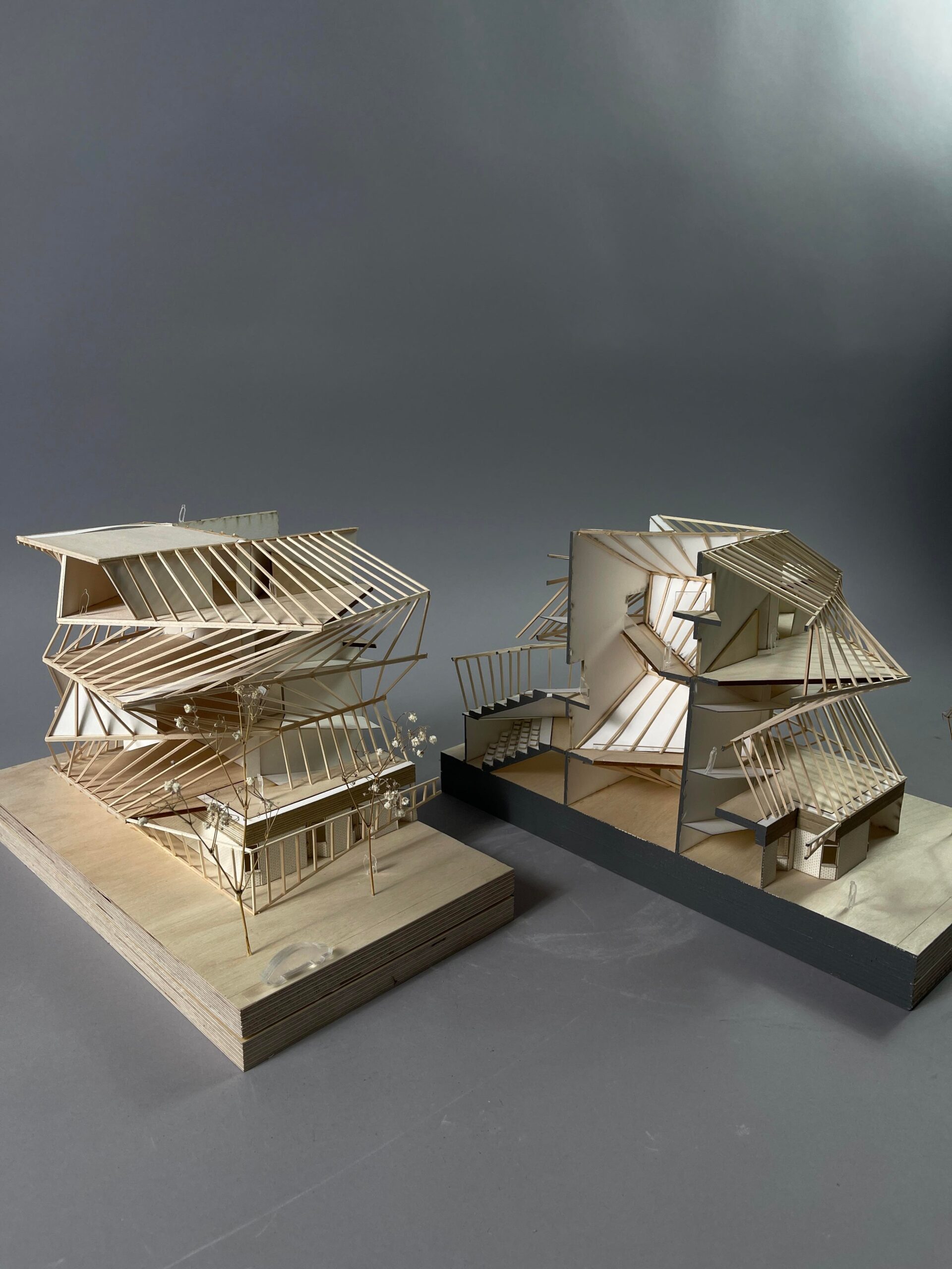 Two 3D models of a multi-leveled structure with terraces framed by angled beams. The models are made of wood. One model shows the entire structure while the other shows a cross section of the structure.
