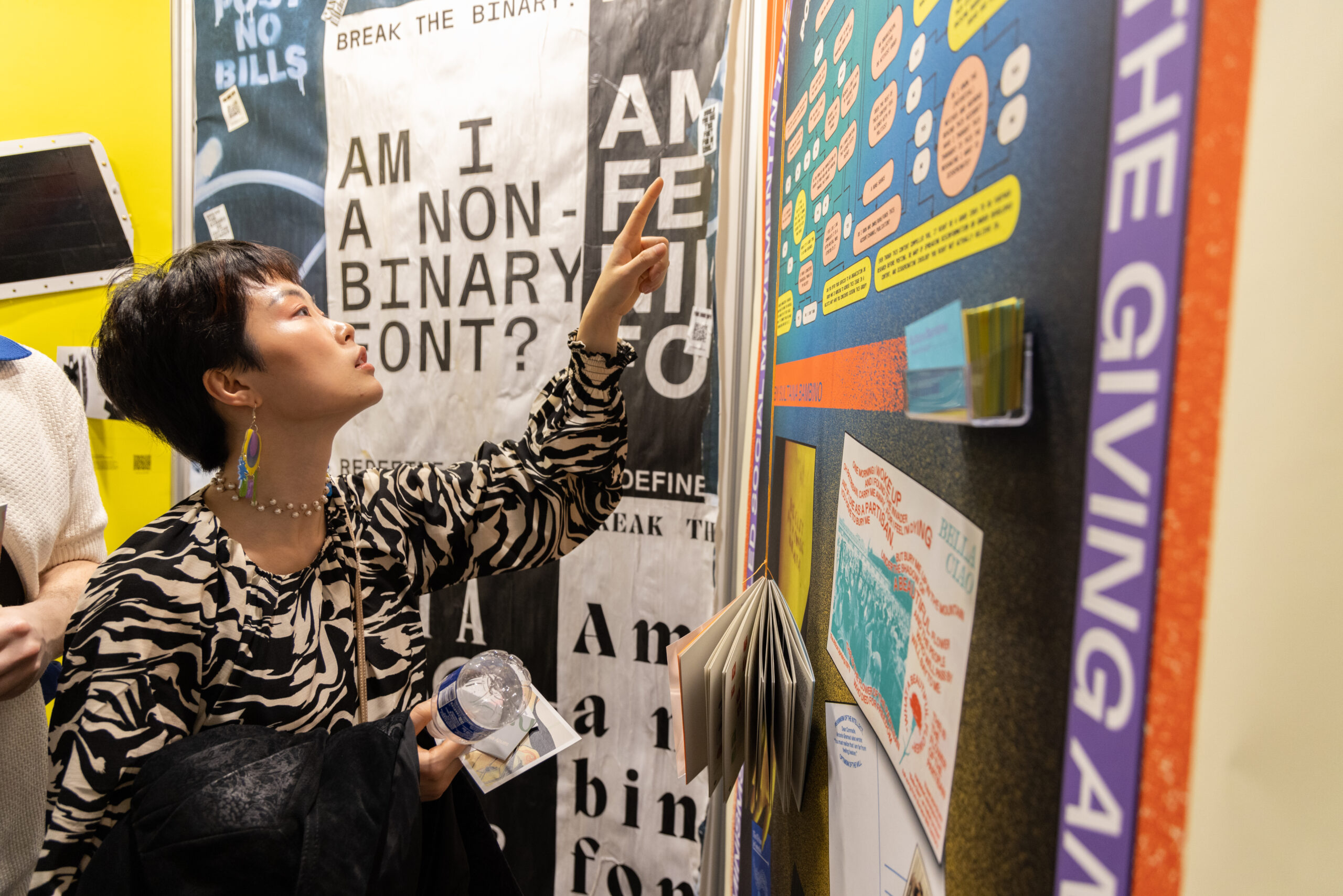 woman examines posters, in gallery room, woman pointing at different posters