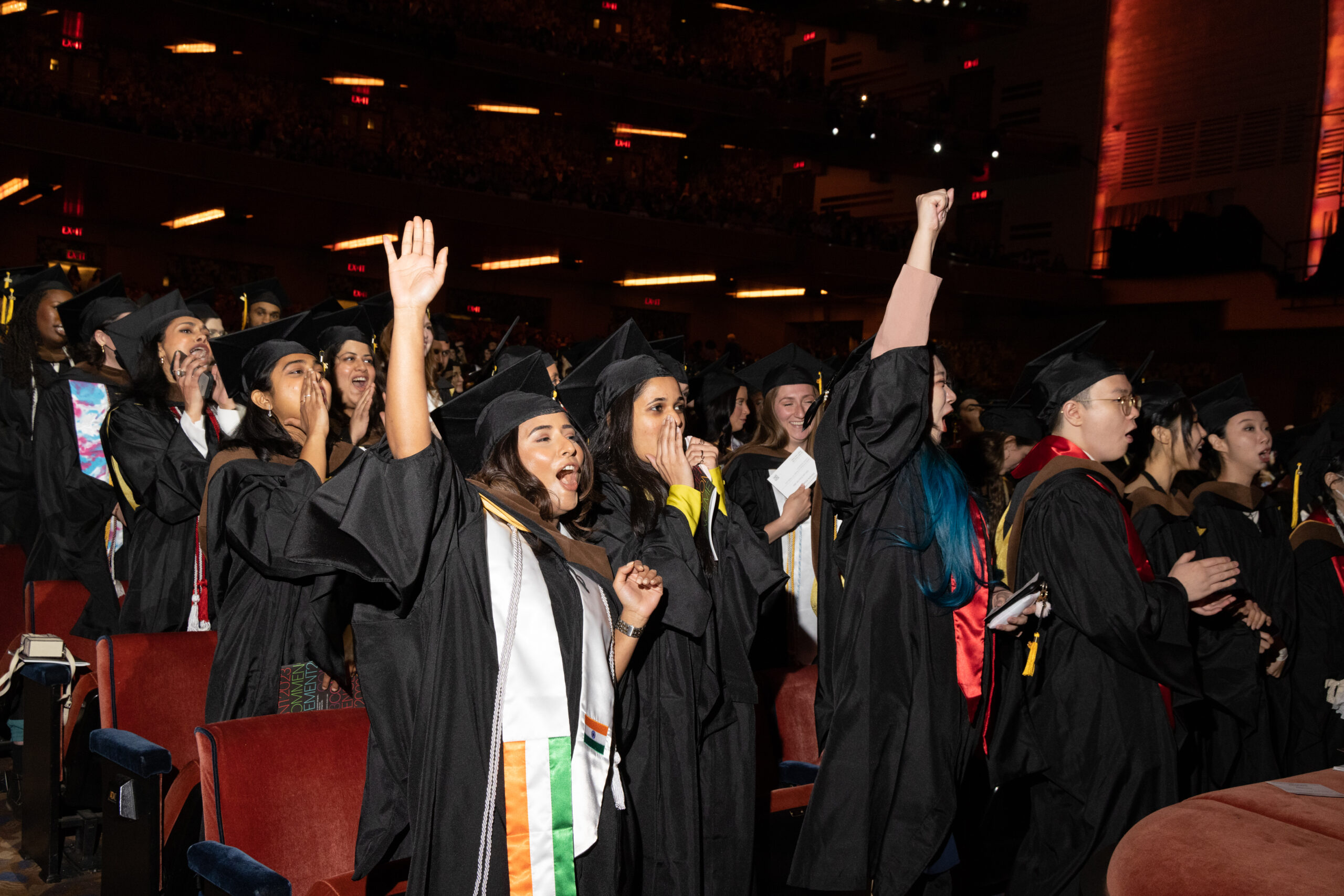 students at commencement, hands raised, and exclaming