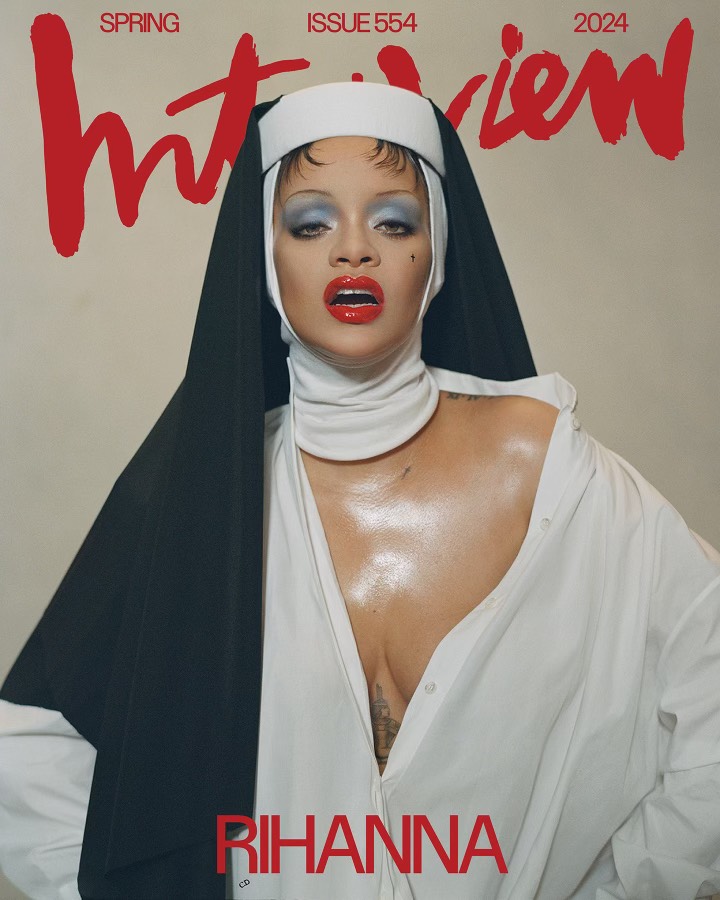A woman in make-up and a loose fitting white button-up top wearing a nun's headdress.