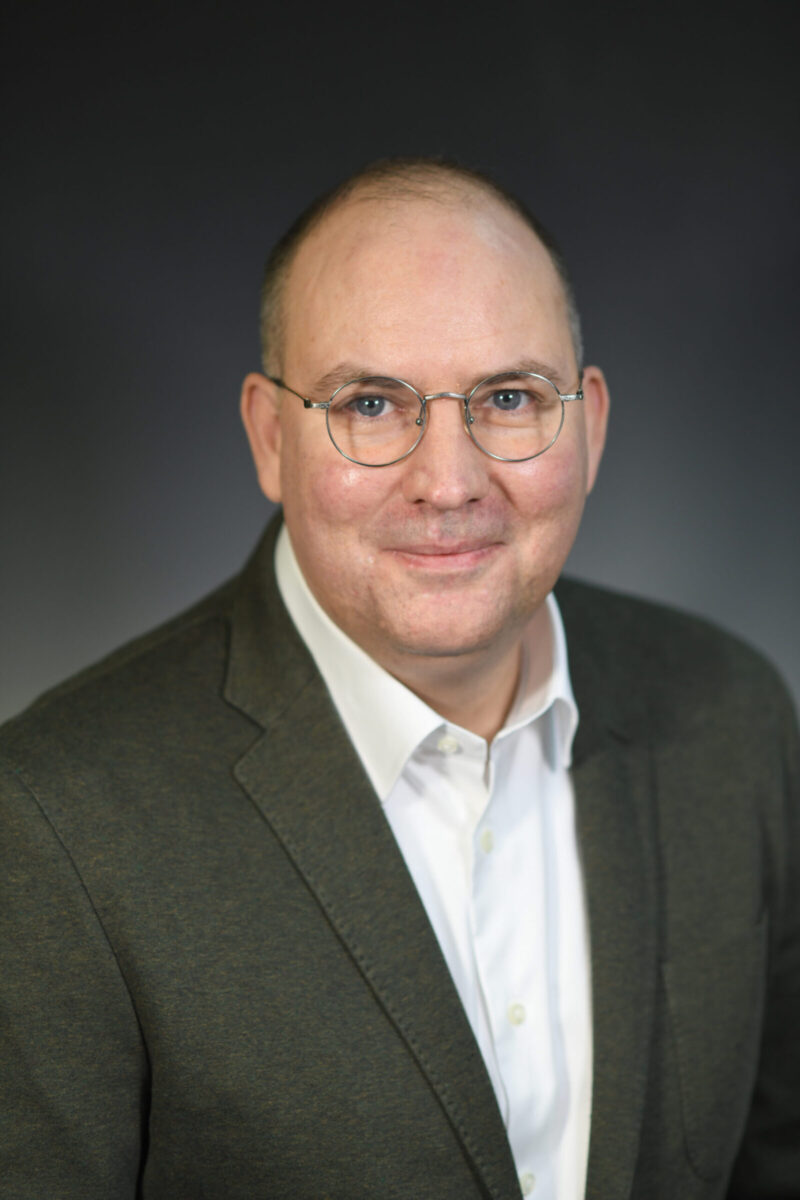 Headshot of new SSCS chair Leo Coleman. He wears a suit and glasses.