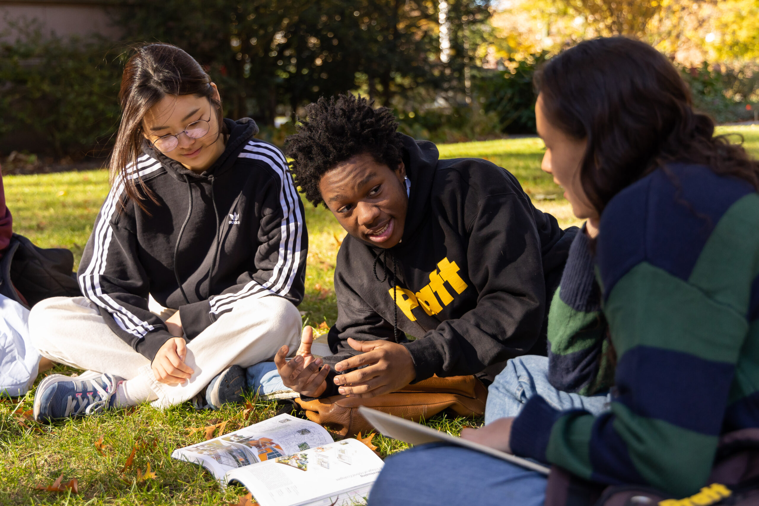 Students sitting on the grass, talking, and looking at a book