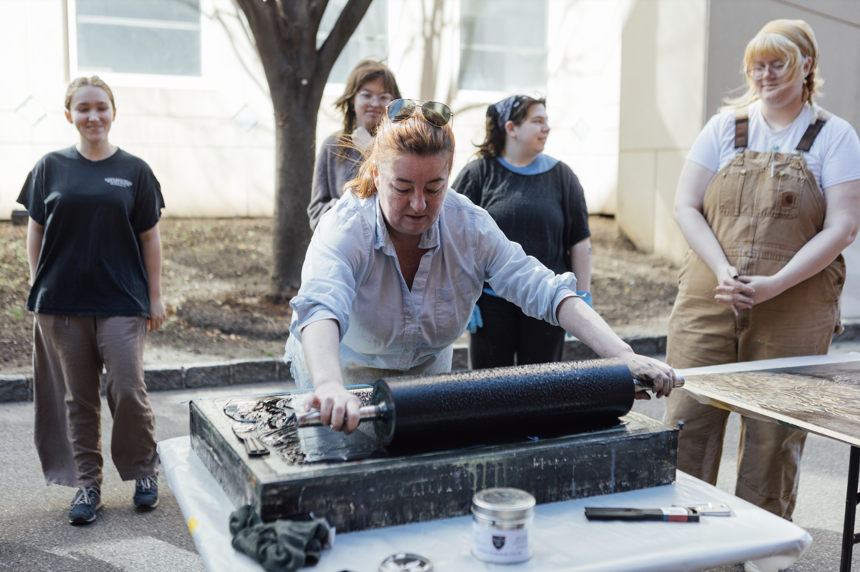 A group of participants watches as a facilitator inks a block with a large roller