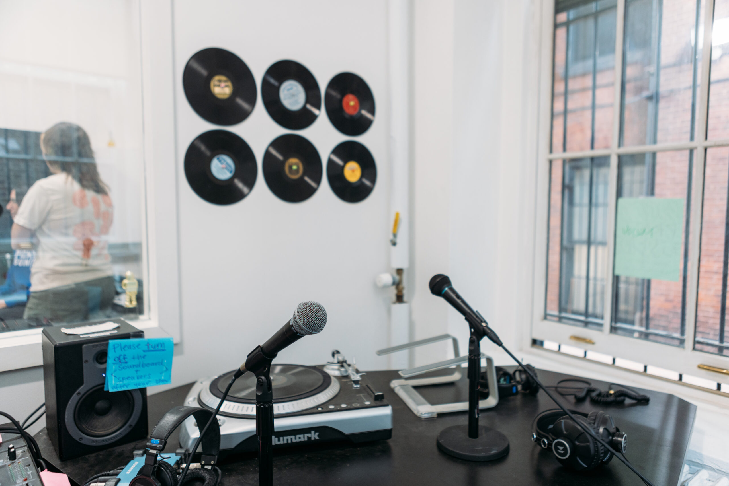 An interior of a white room with two microphones, a record player, and vinyl records on the wall