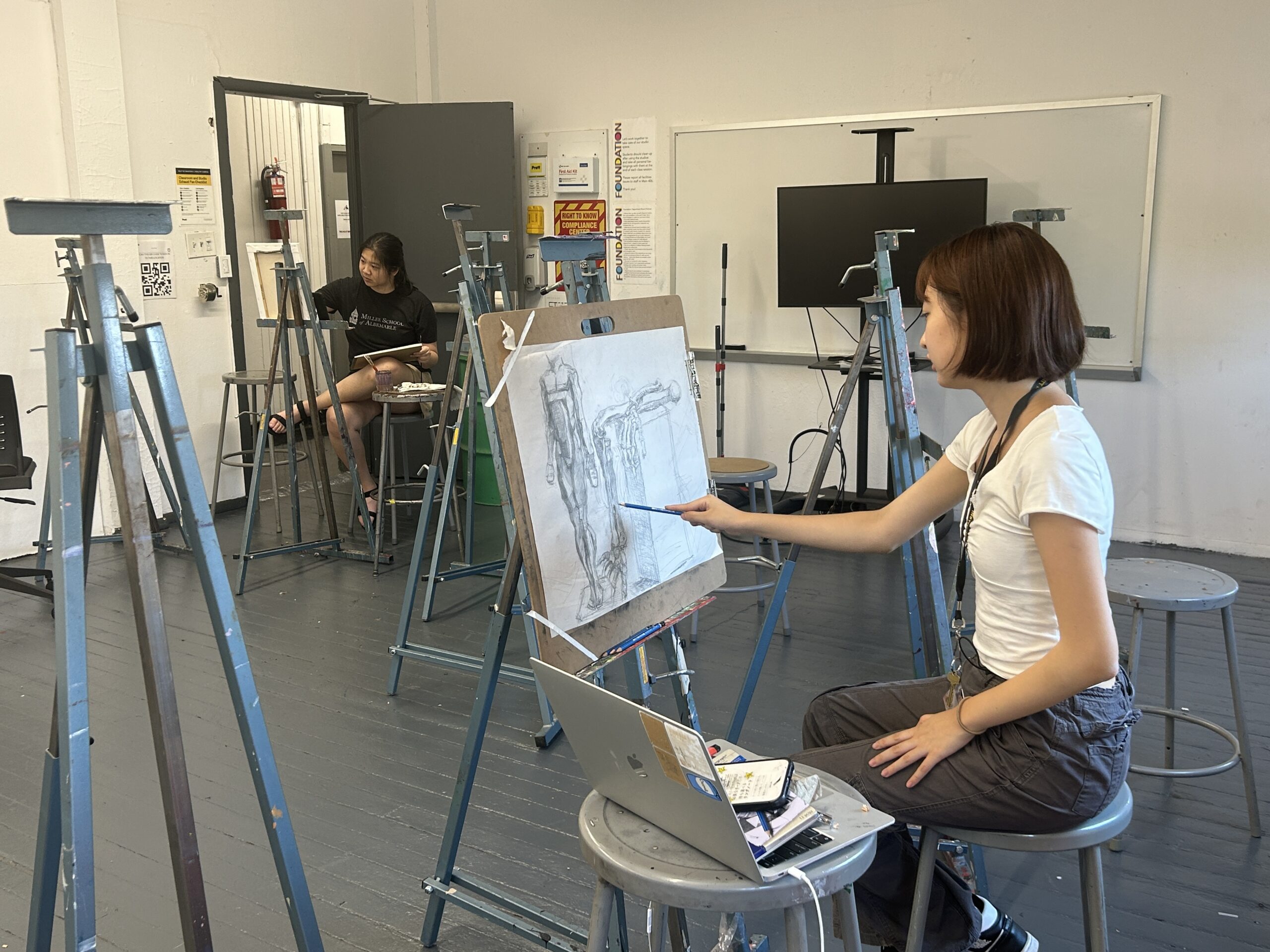 Profile of high school student wearing headphones sitting in front of easel and painting.