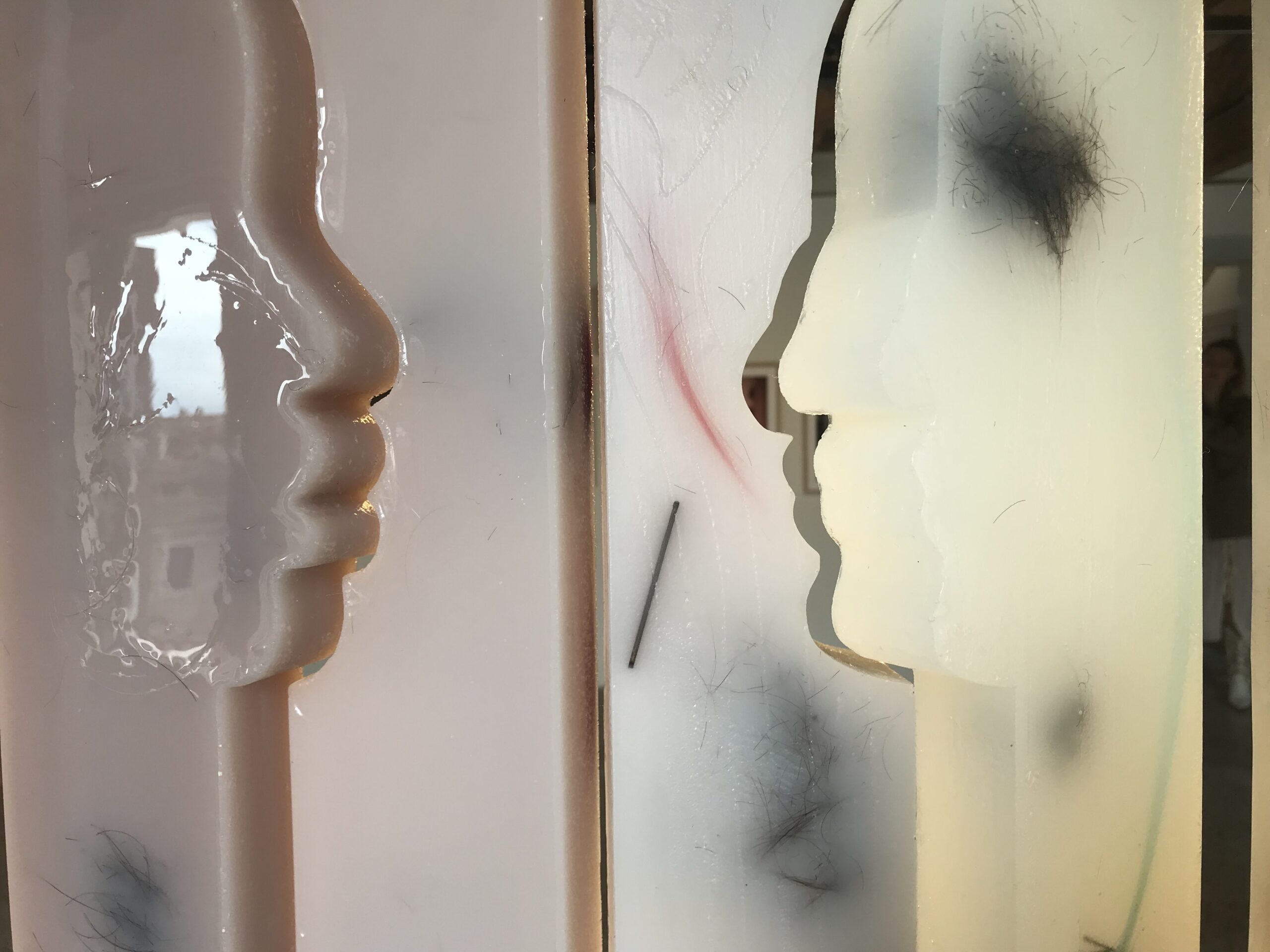 A detail of Face-Ade, which shows two silhouettes facing one another cut out of the material. Clumps of hair are embedded in the material.