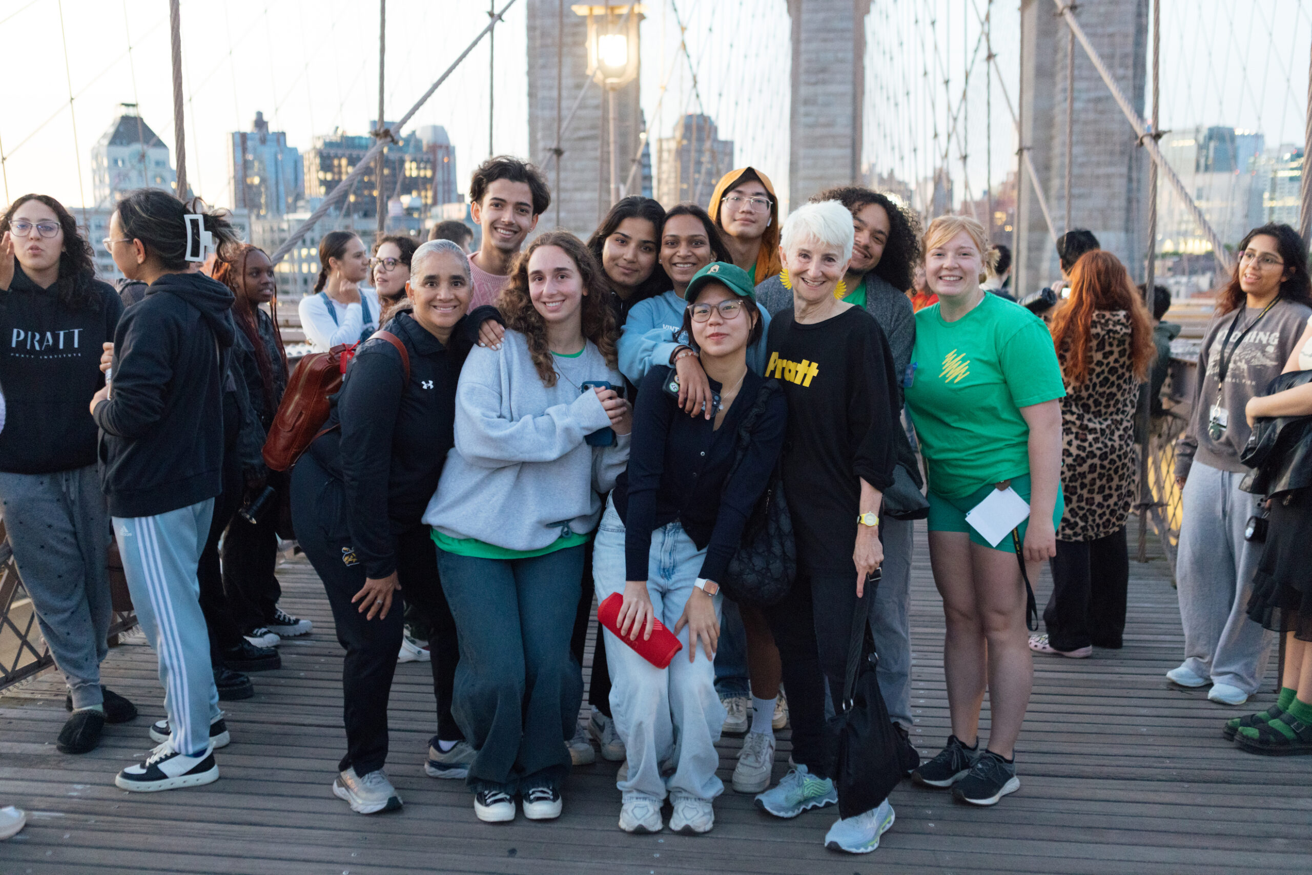 Students and administrators pose smiling with President Frances Bronet on the Brooklyn Bridge at sunrise