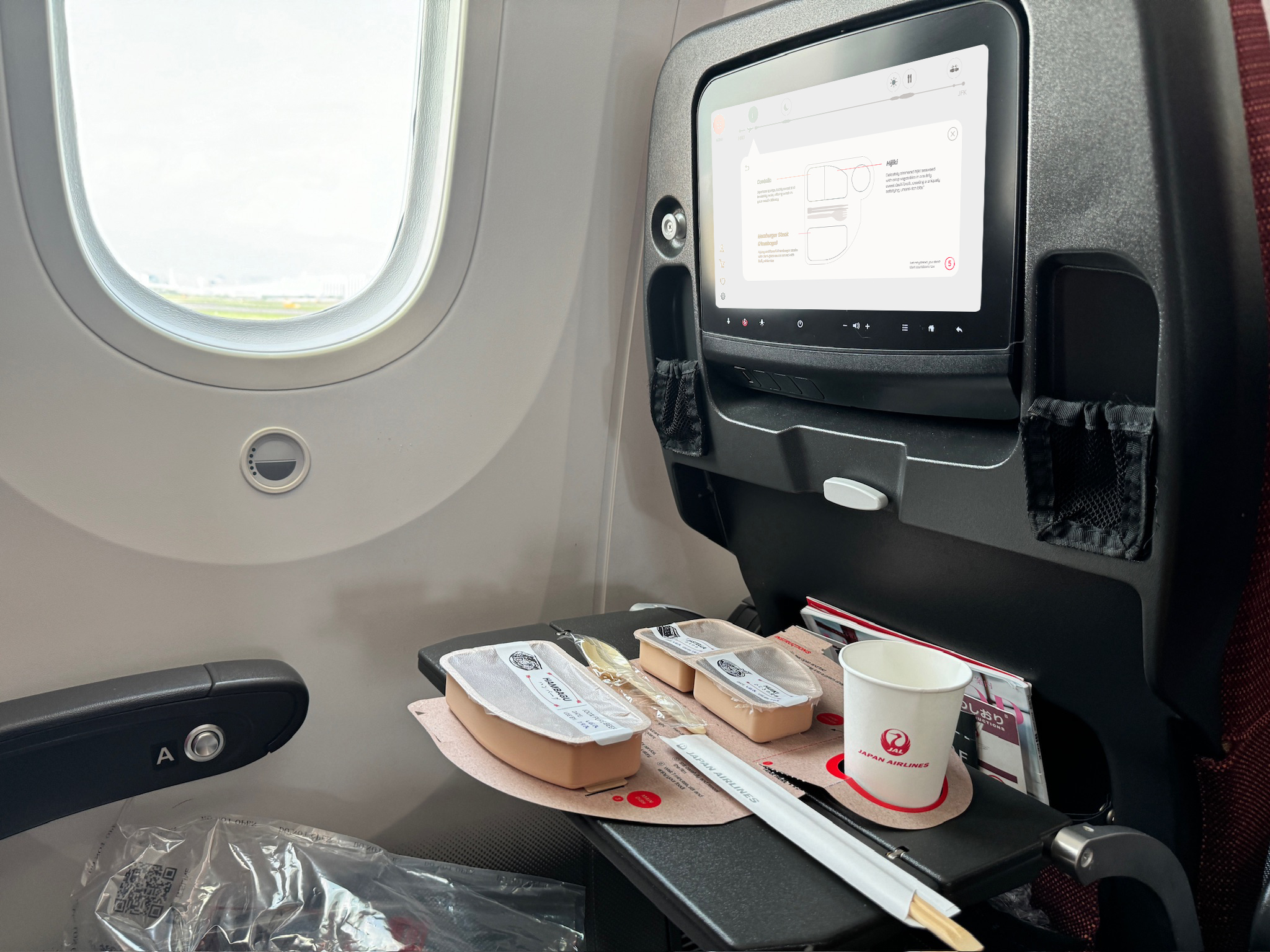 Sorajin packaging including sealed food trays, chopsticks, and a cup open on an airplane tray table.