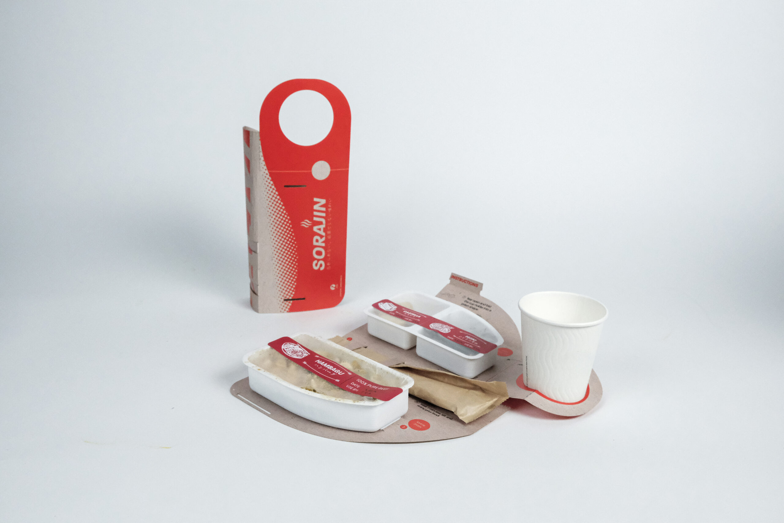 A fold-out cardboard container with pre-packaged food trays and paper cup on a white background.