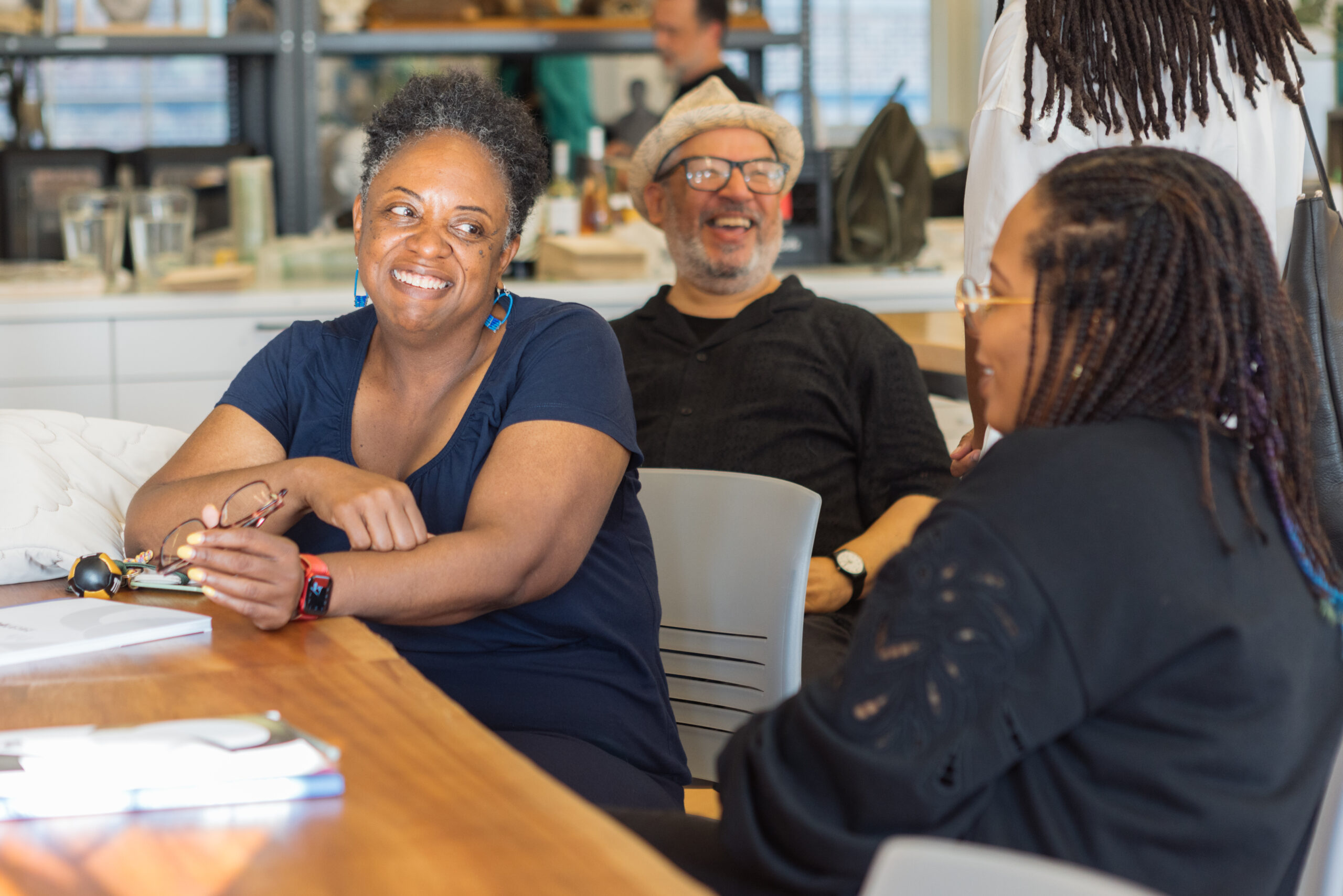 Close-up of four people, three of whom are seated and one standing slightly out of frame, in a bright room