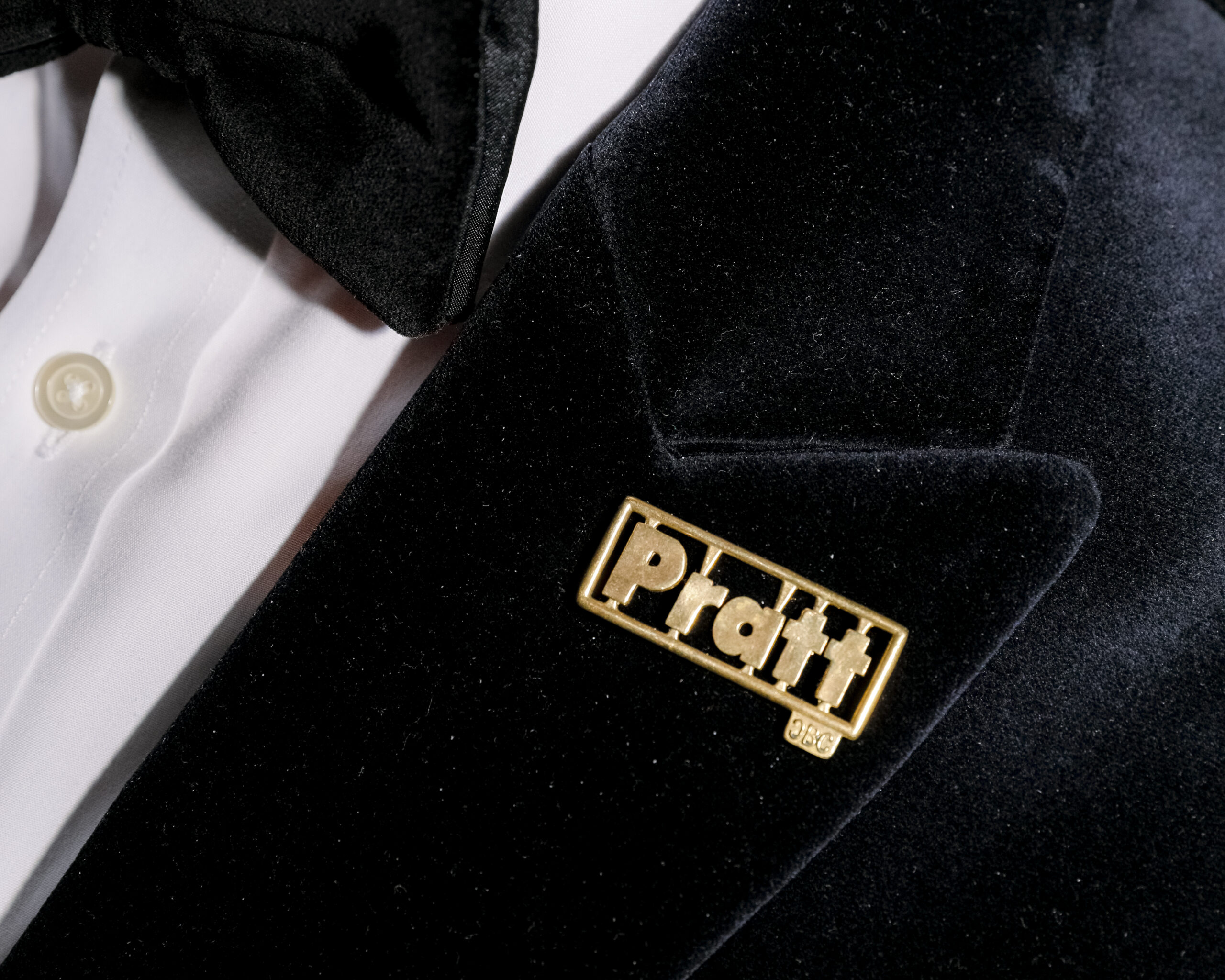 Close up of a gold Pratt pin on a black suit.