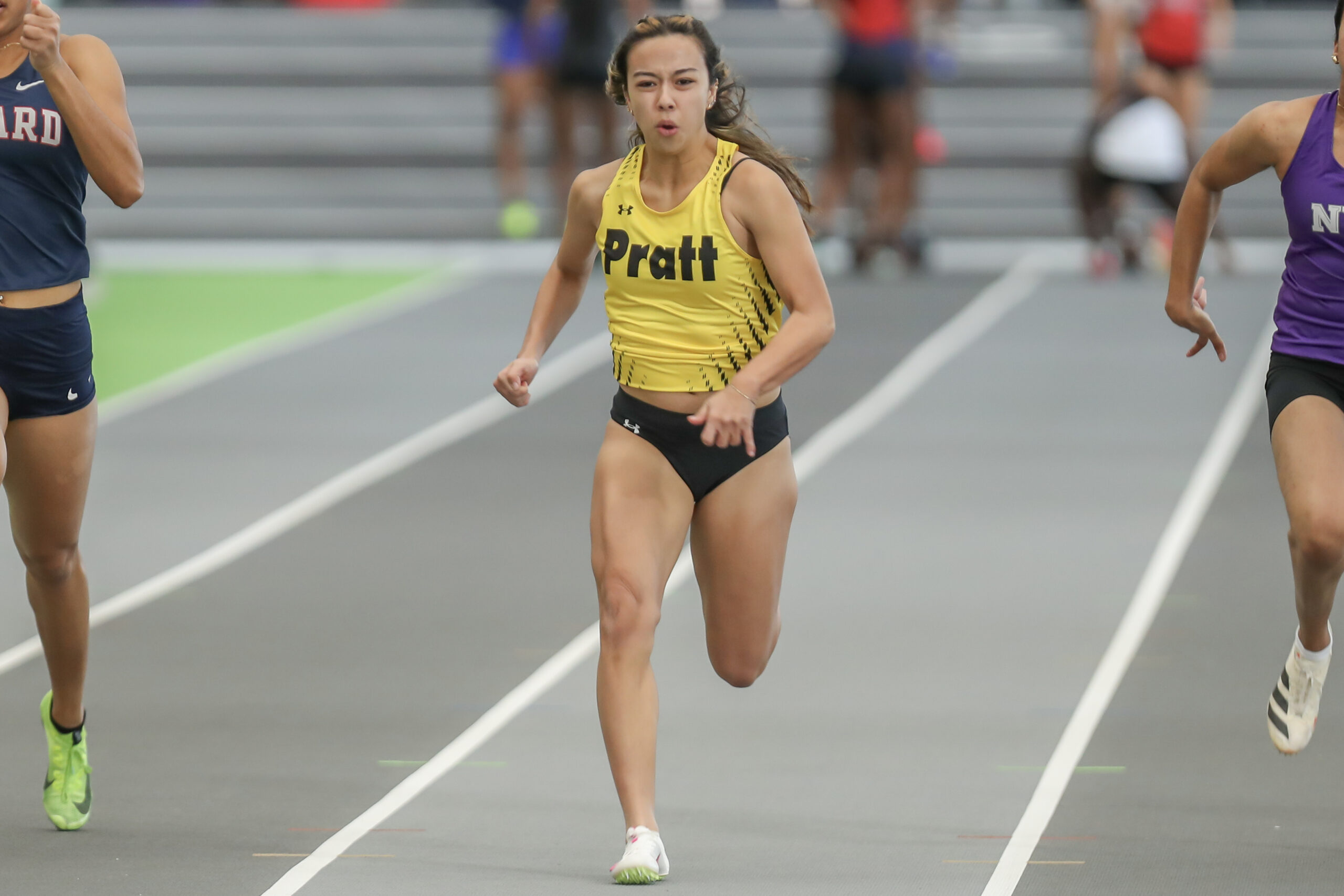 A runner in a Pratt uniform competes against two other runners on a track.