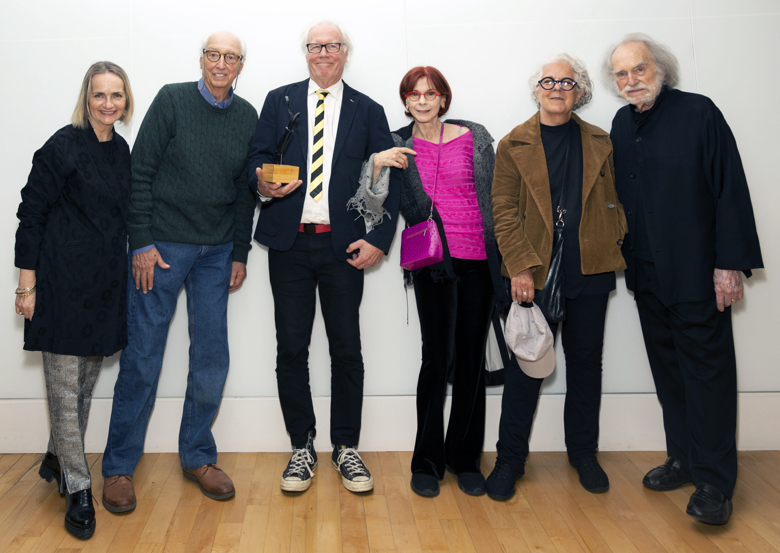 Six people pose smiling for a photo, with the third from left holding an award