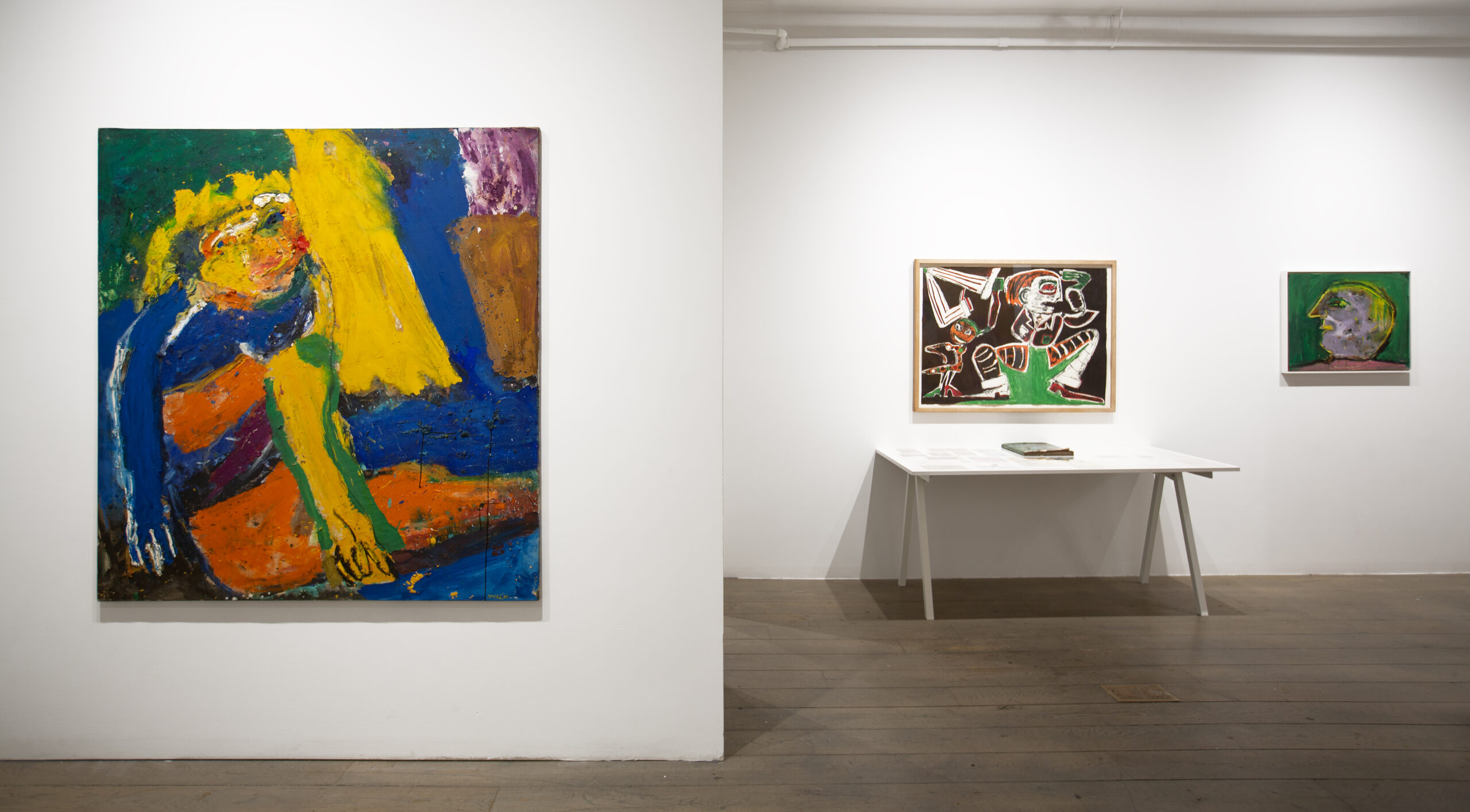 Three paintings with bright colors, all different sizes, hang on a white gallery wall