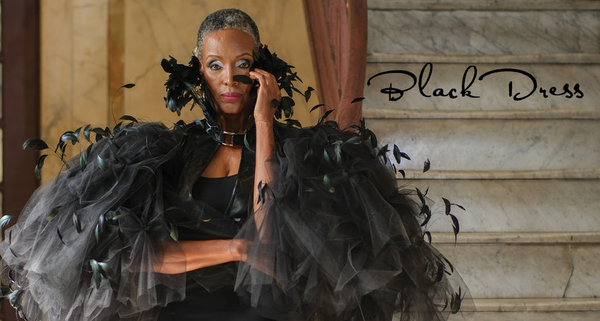 A black woman wearing a poofy black dress with black feathers on it, and the text