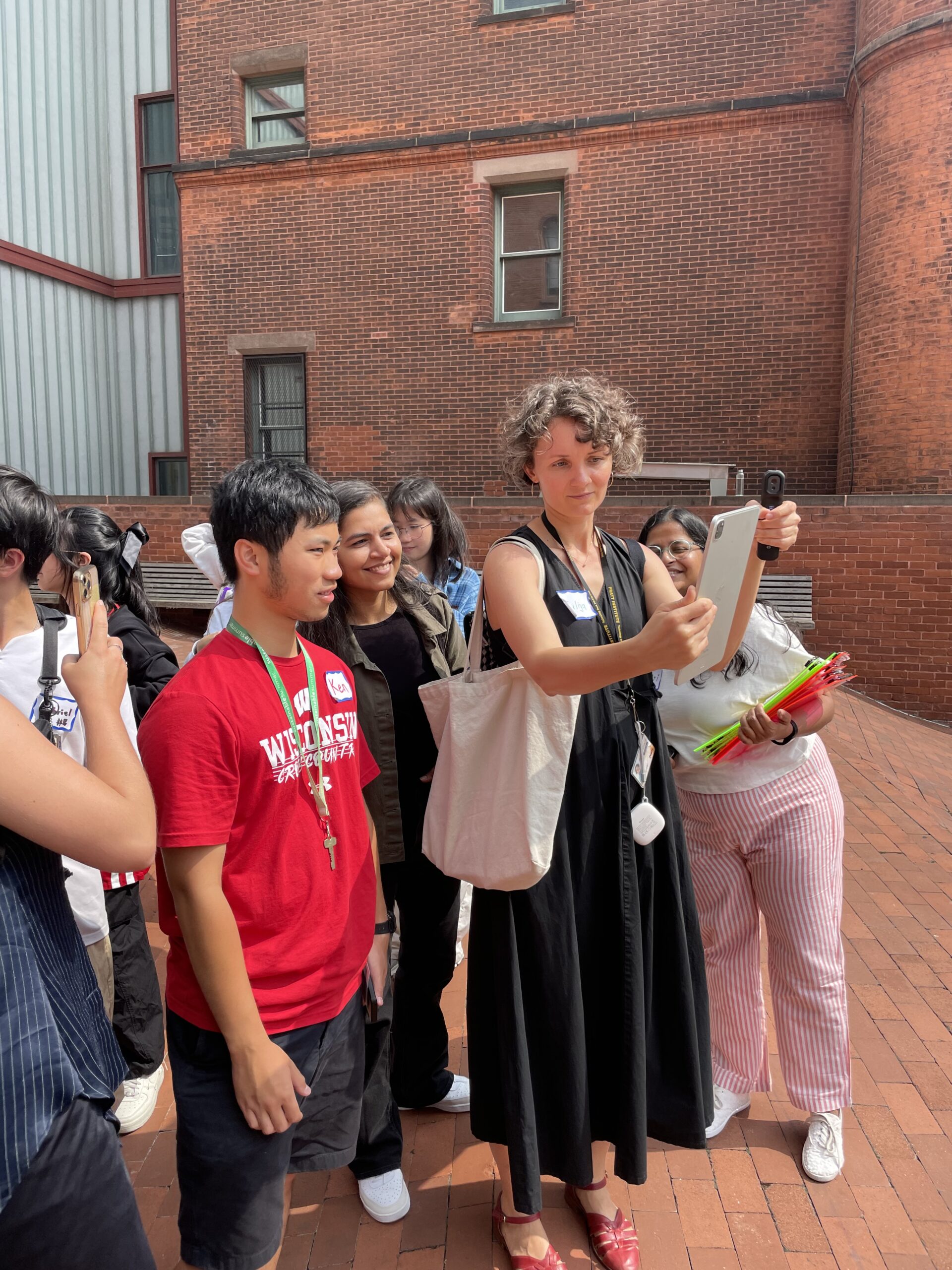Students gather around Dzuyban to look at the tablet she holds in a brick campus courtyard