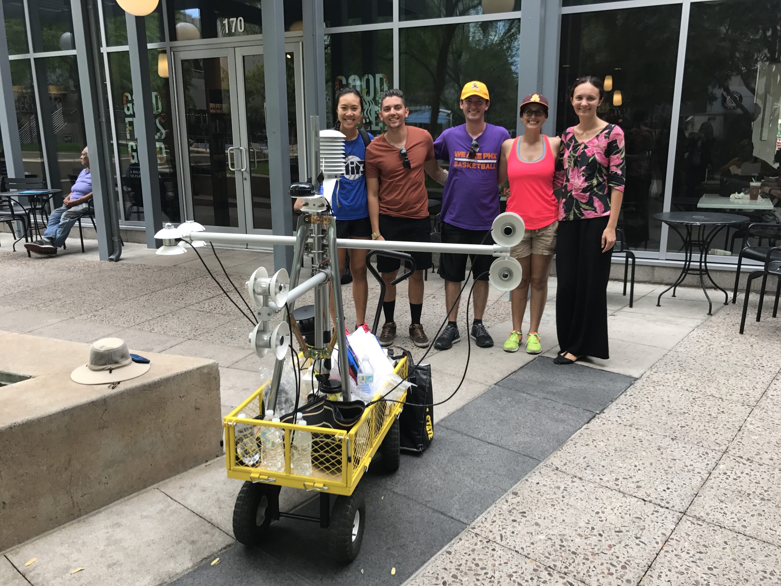 A group of five people stand behind a cart which contains a device with long horizontal arms used to measure heat