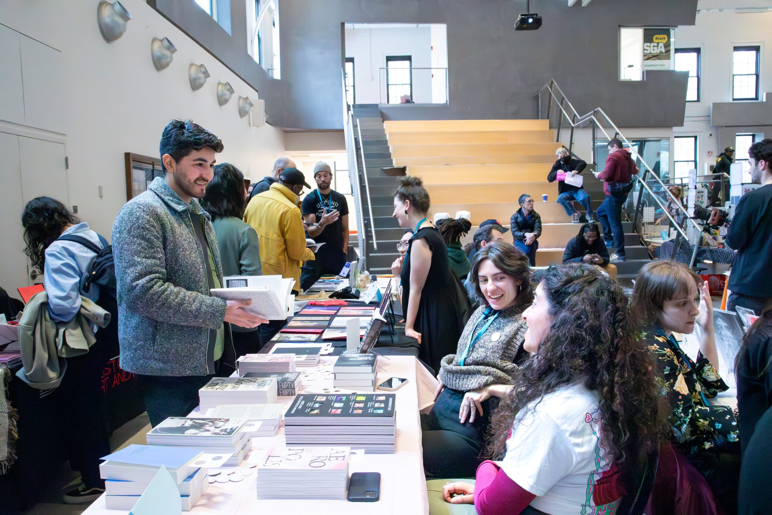 Vendors and attendees smile and talk to each other across tables where printed materials are arranged