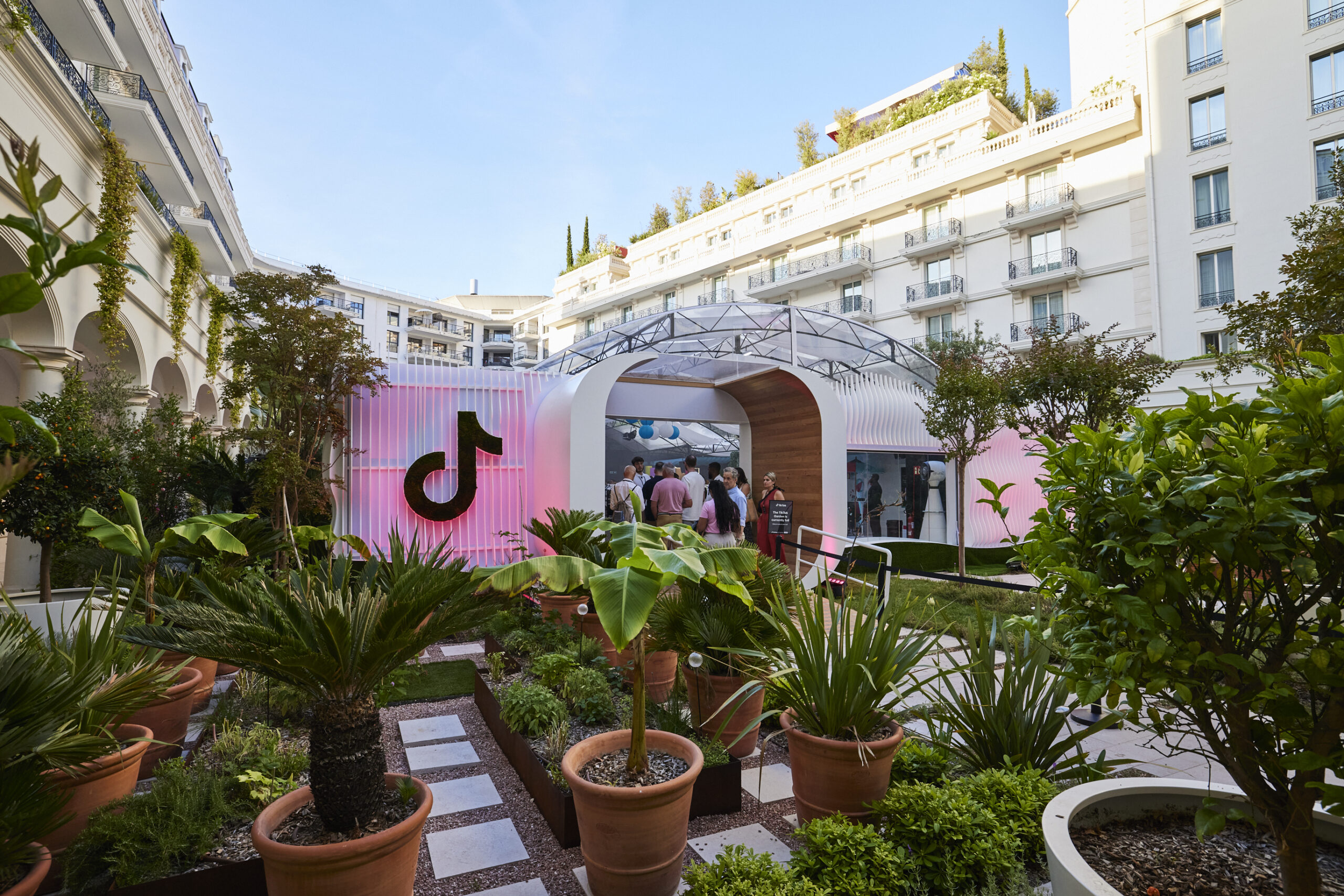 Covered structure with the TikTok logo in the center of the frame in a sunny, plant-filled courtyard.