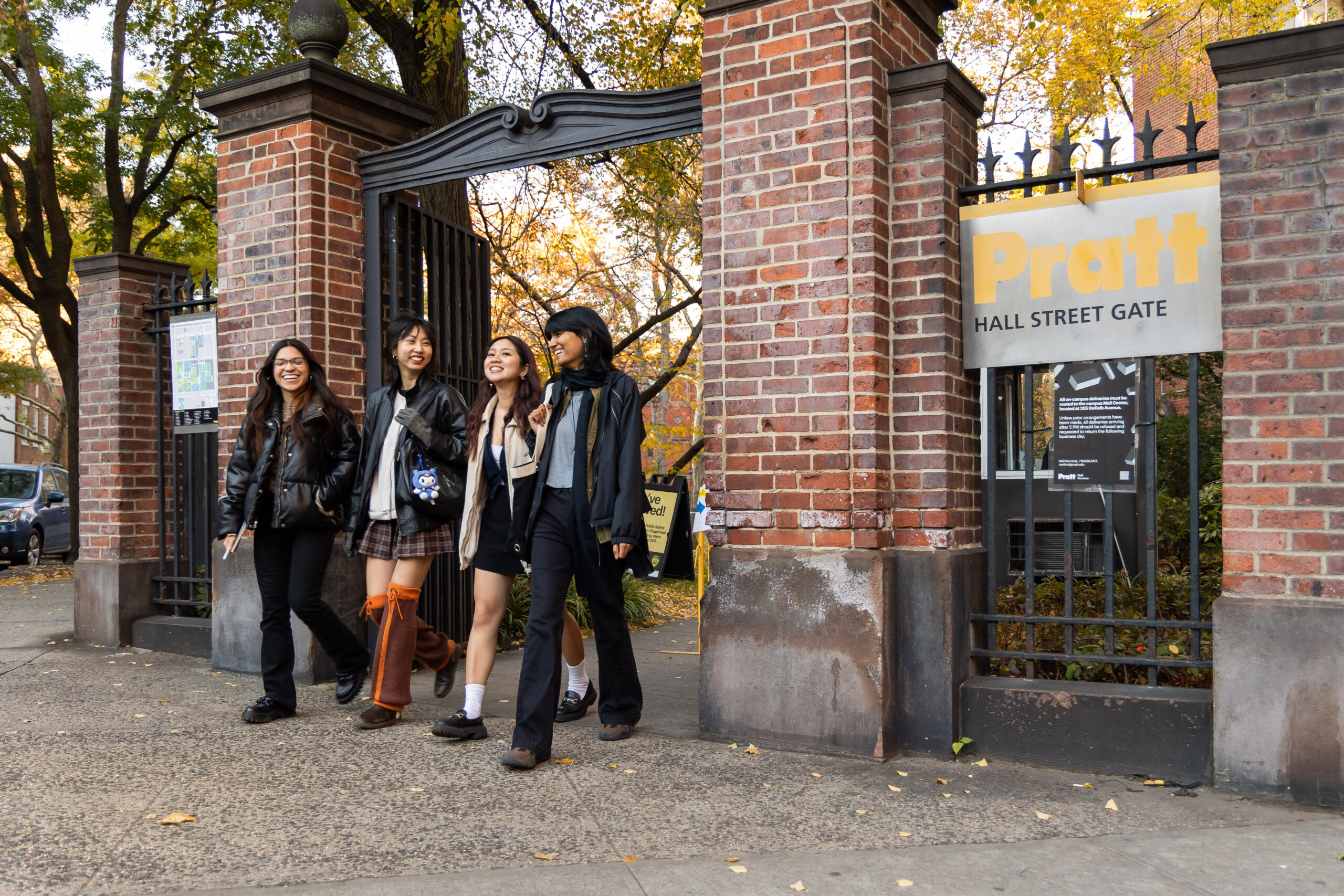 Four young people are walking together through a brick gate with an arch labeled 
