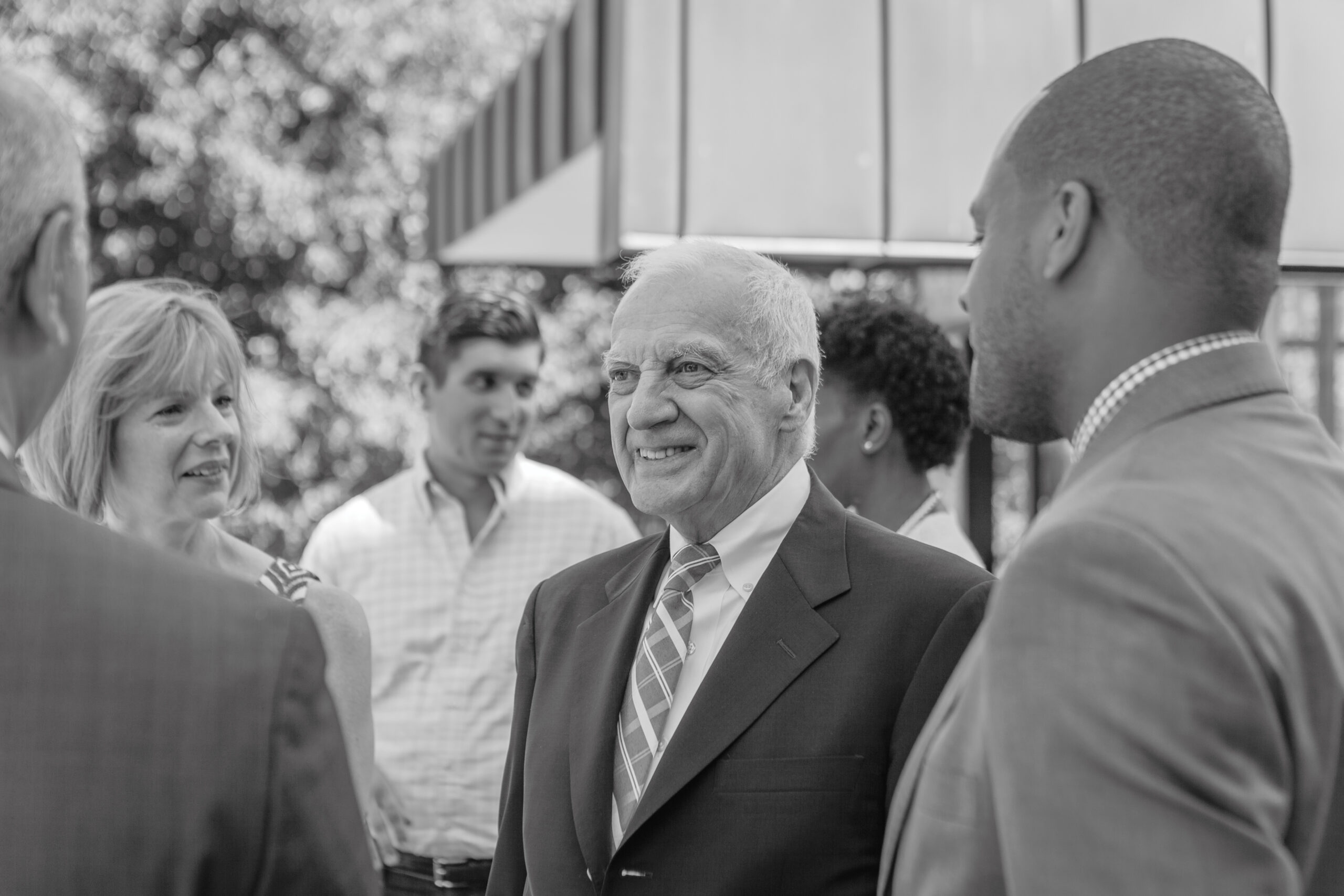 Black-and-white image of Dr. Schutte smiling, encircled by fellow leaders and members of the Pratt community
