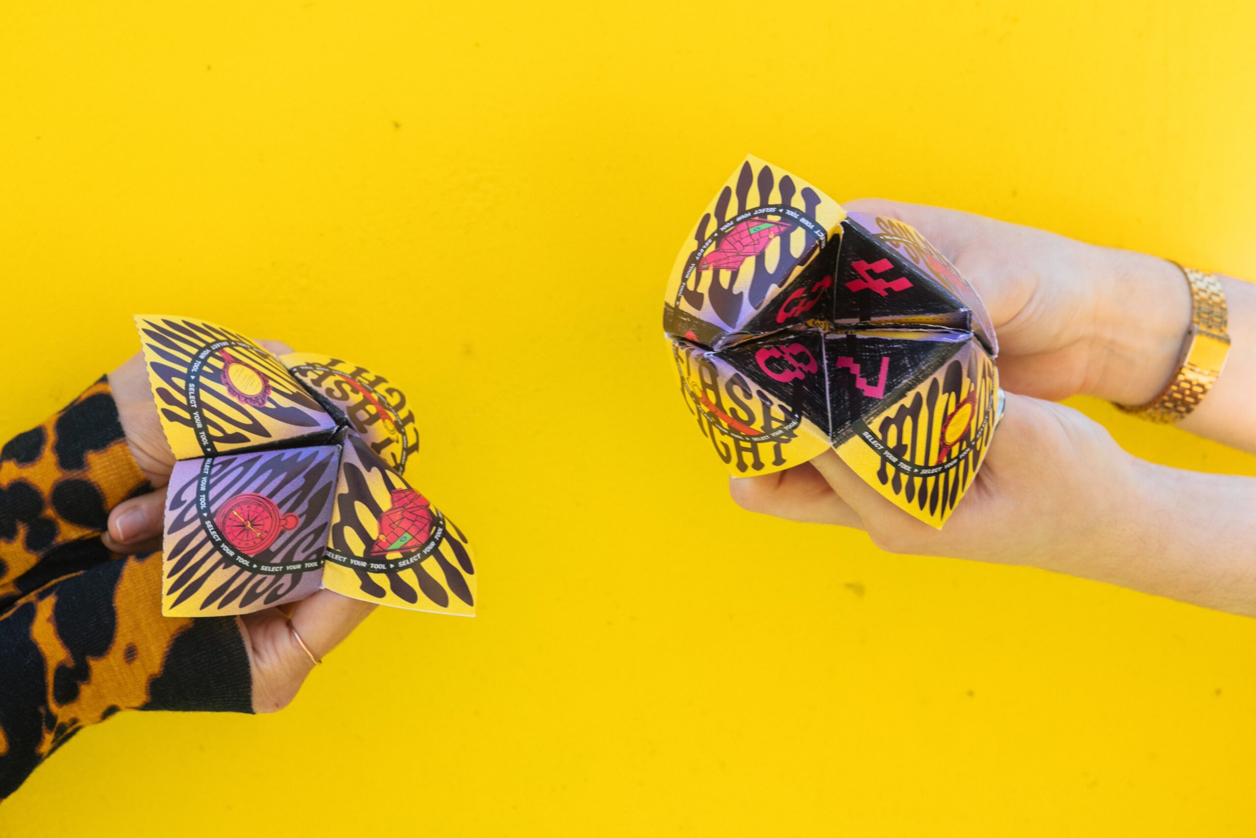 Two hands holding folded-paper fortune tellers against a bright yellow background