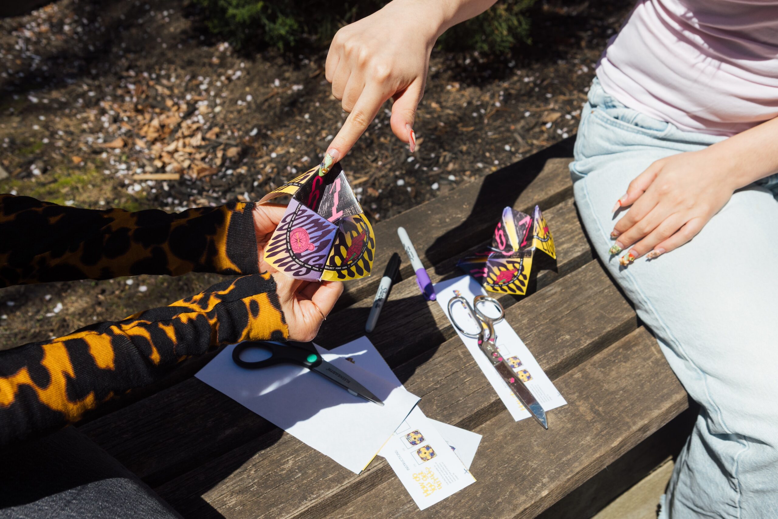 Close-up of two people's hands: one holds the paper fortune teller, arms outstretched, while the other points to it