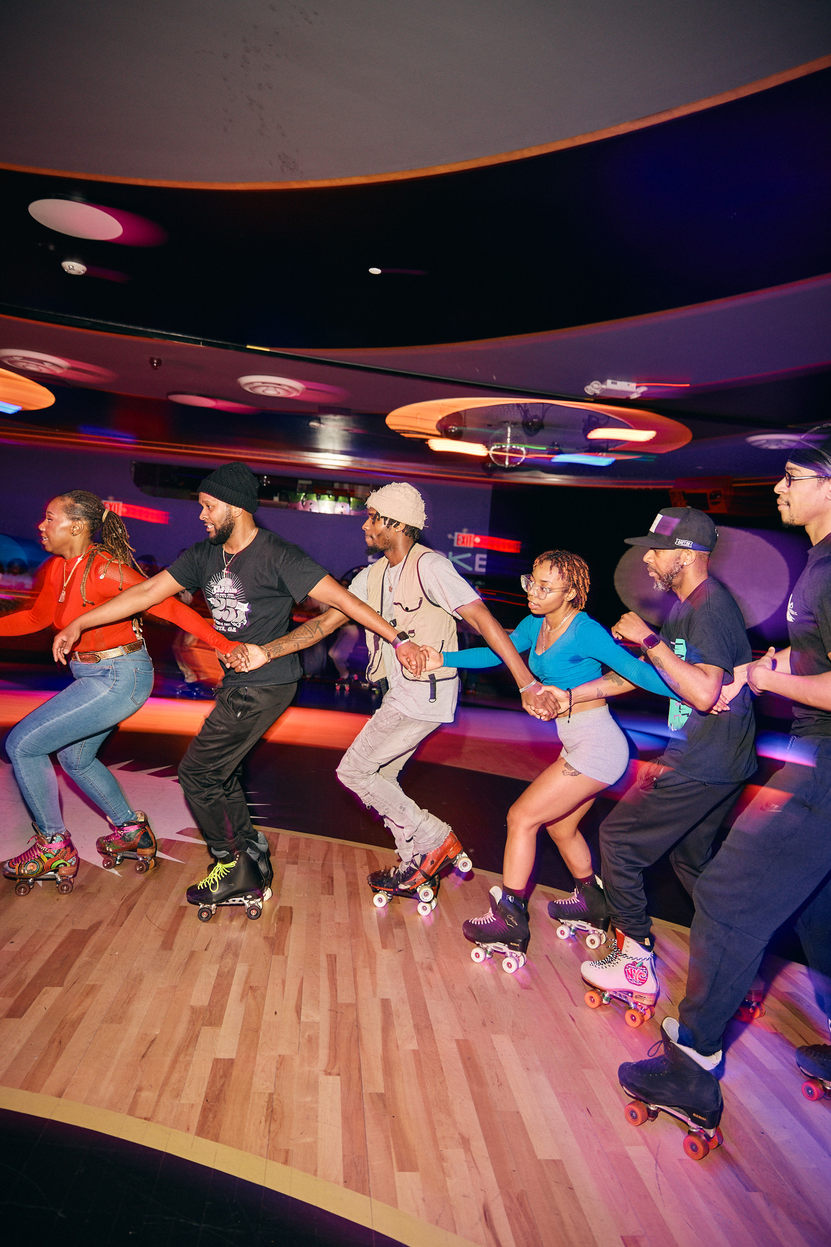 A group of five people on inline roller skate in an indoor rink, linking arms to form a line