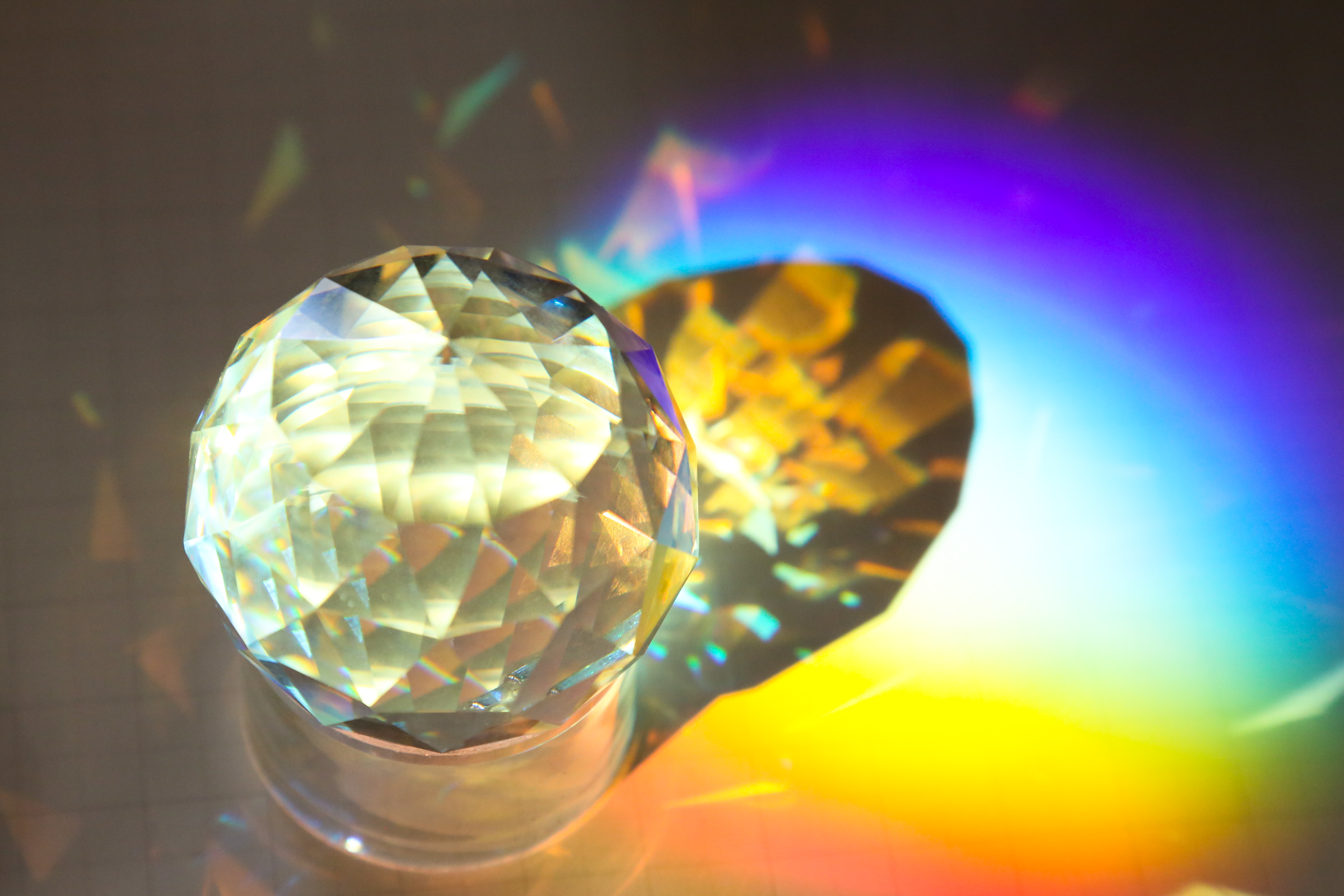 A circular prism casting a rainbow, light refracting onto the surface where it sits