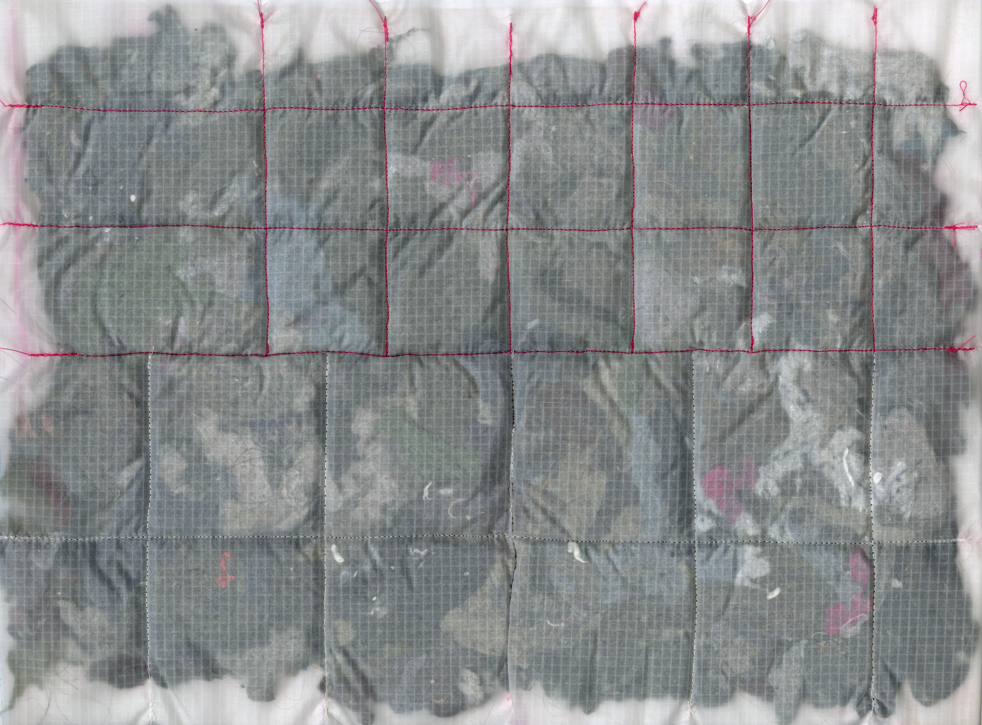 A close-up of a translucent textile quilted with red thread into square segments. Underneath the fabric, clusters of grey felted lint are visible, creating a textured, layered effect.
