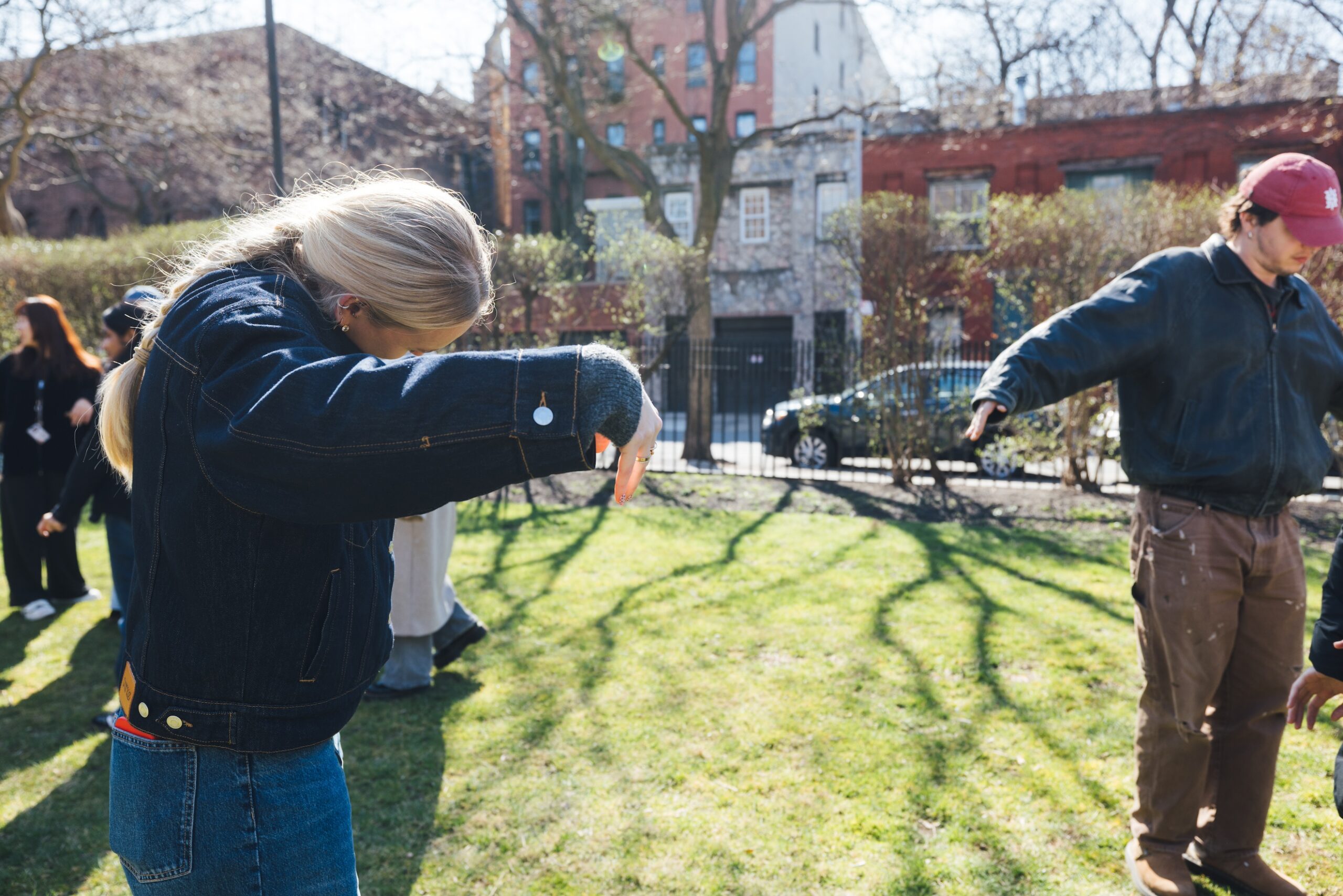Two students stand and meditatively move their arms on a sunny, grassy campus lawn