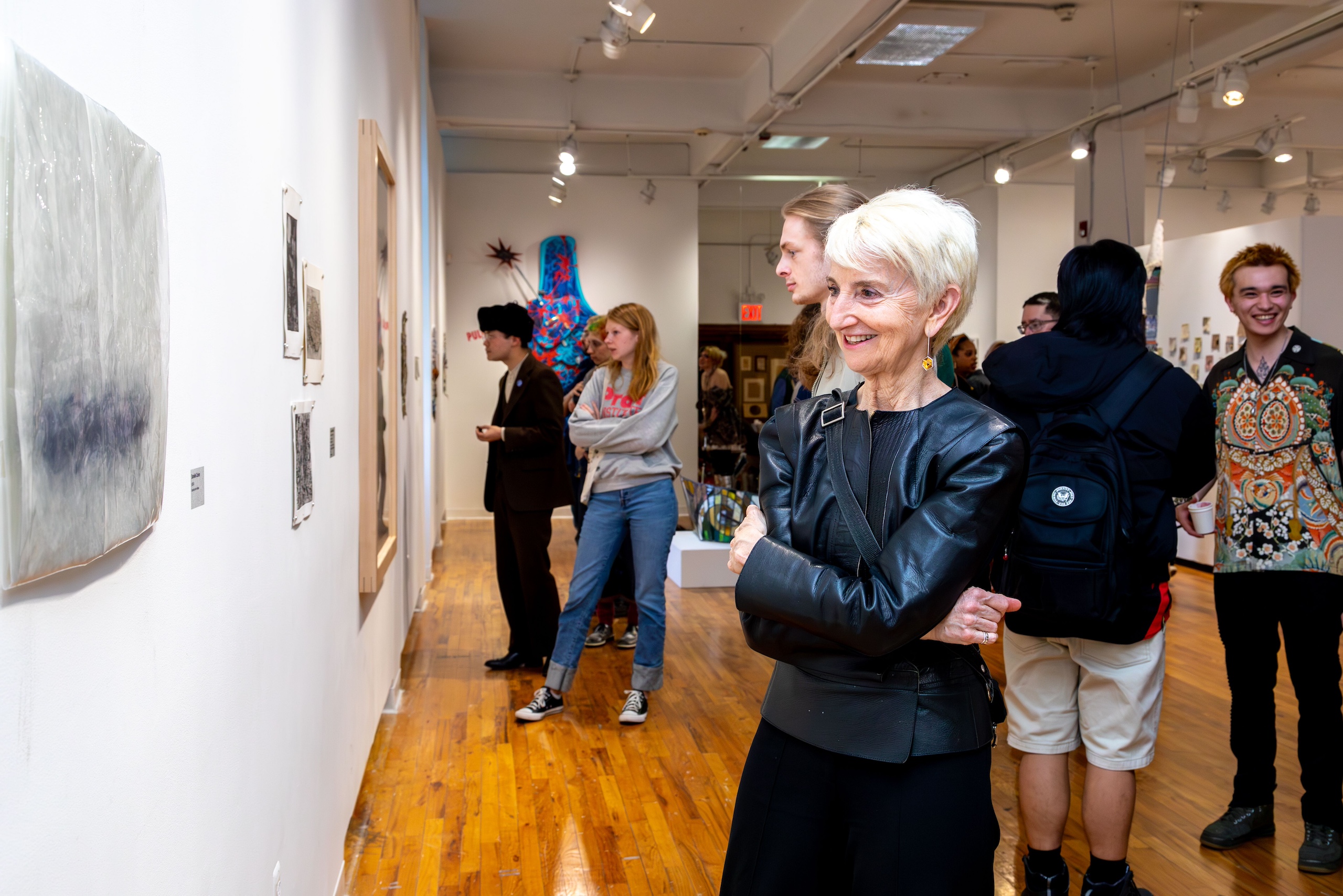 President Frances Bronet smiles looking at student artwork installed in a gallery among students
